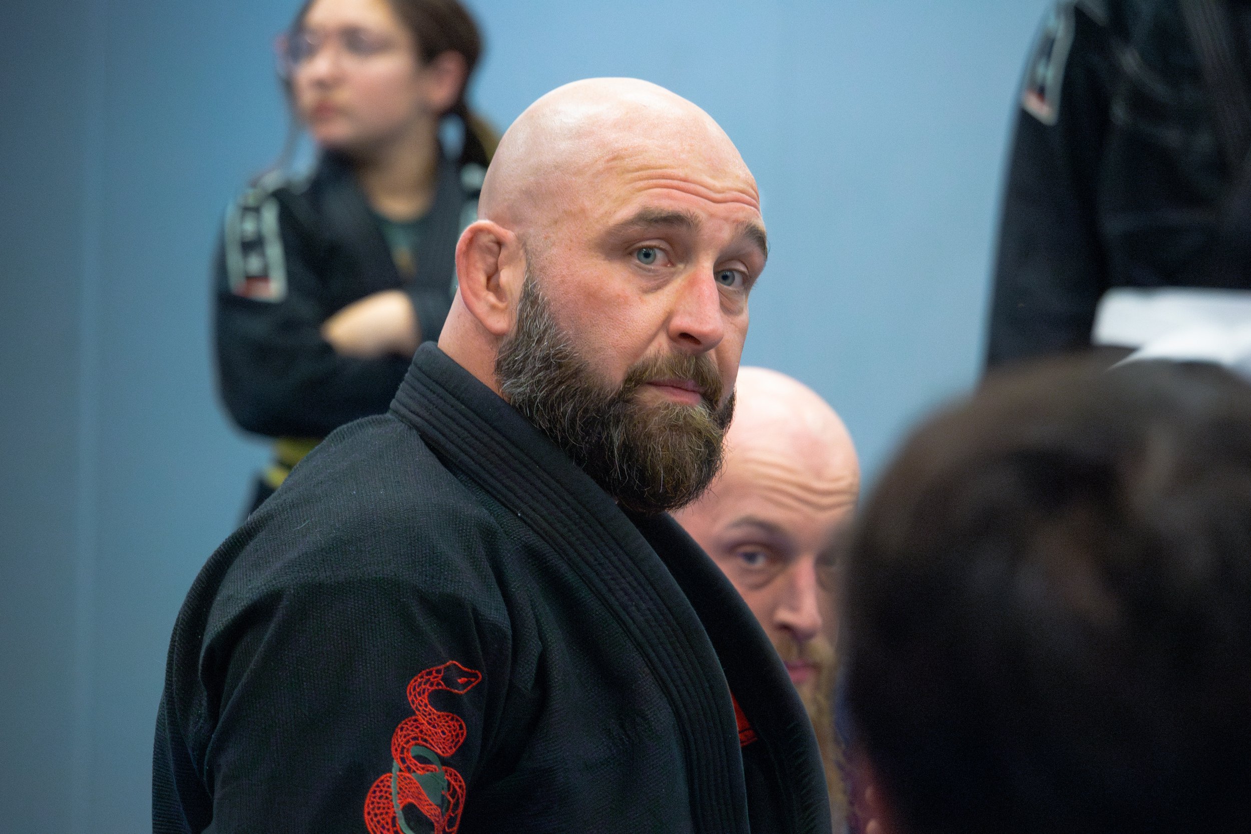 Bald man with beard in jiu-jitsu gi at martial arts class.