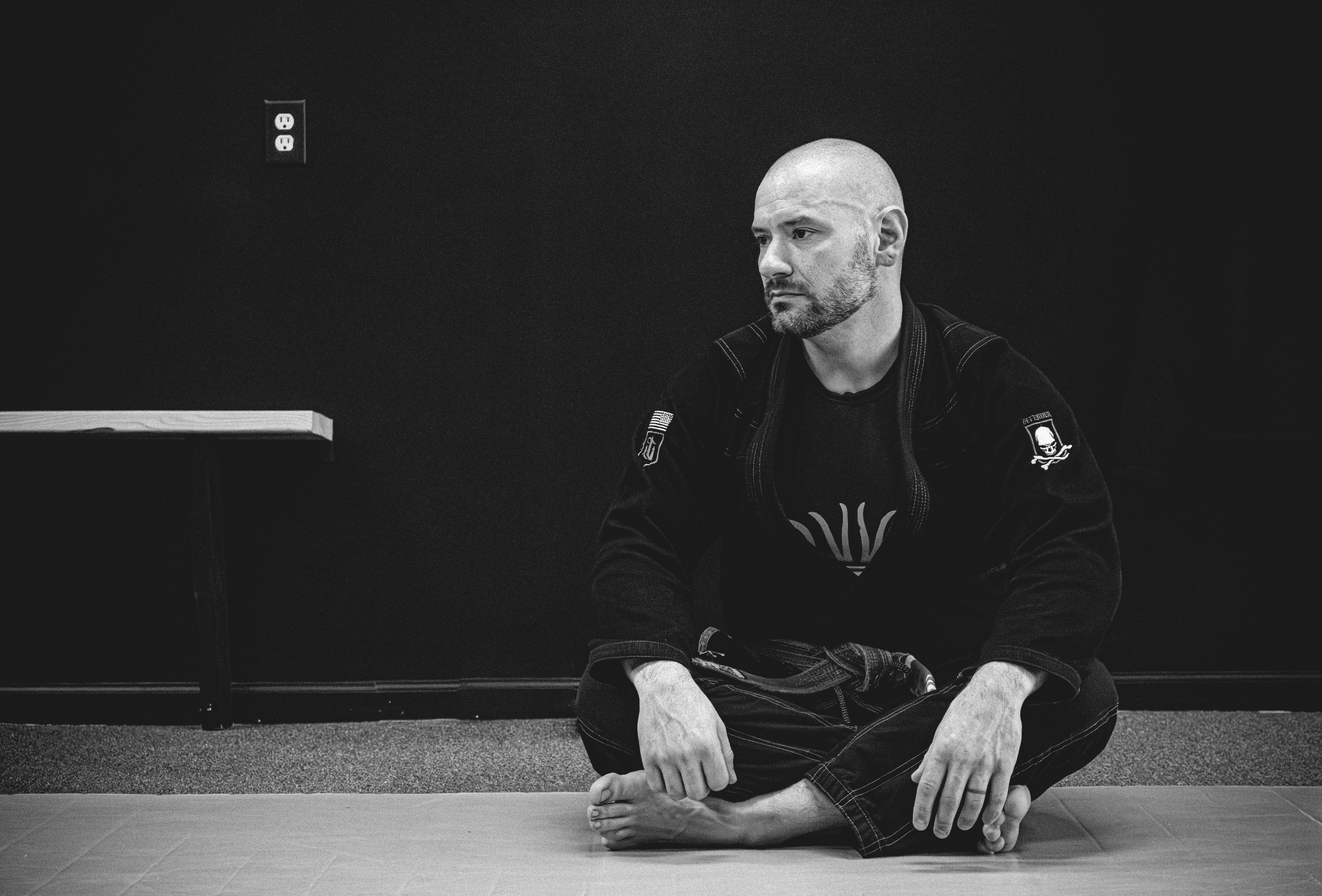 Man in a martial arts gi sitting on a mat in a dojo.