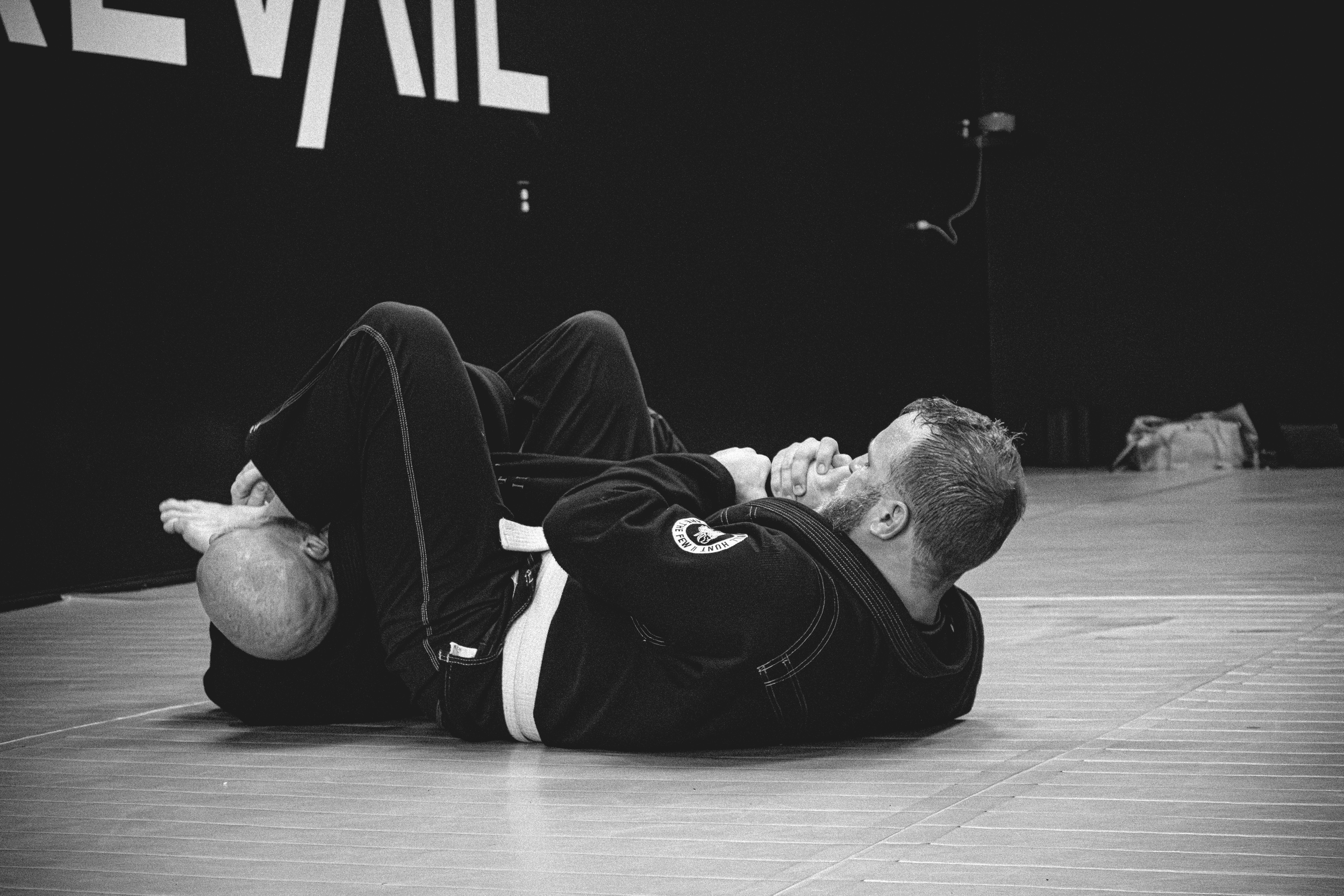 Two people practicing Brazilian Jiu-Jitsu on a mat, engaged in a grappling position, wearing gis.