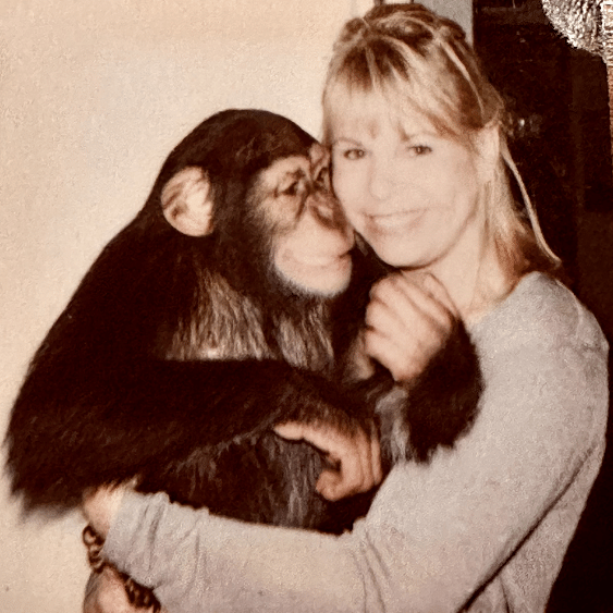 A woman holding and hugging a baby chimpanzee indoors.