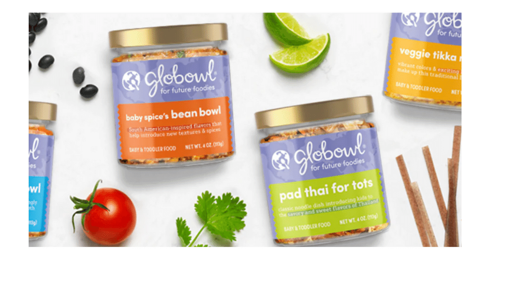 Several jars of Globowl baby and toddler food flavors, including baby spice's bean bowl and pad thai for tots, garnished with lime wedges, a cherry tomato, cilantro, and some breadsticks on a white background.