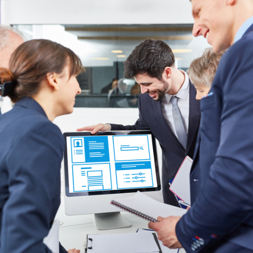 Group of business professionals in a meeting room reviewing a computer screen displaying digital interface designs. They are smiling and engaging in discussion.