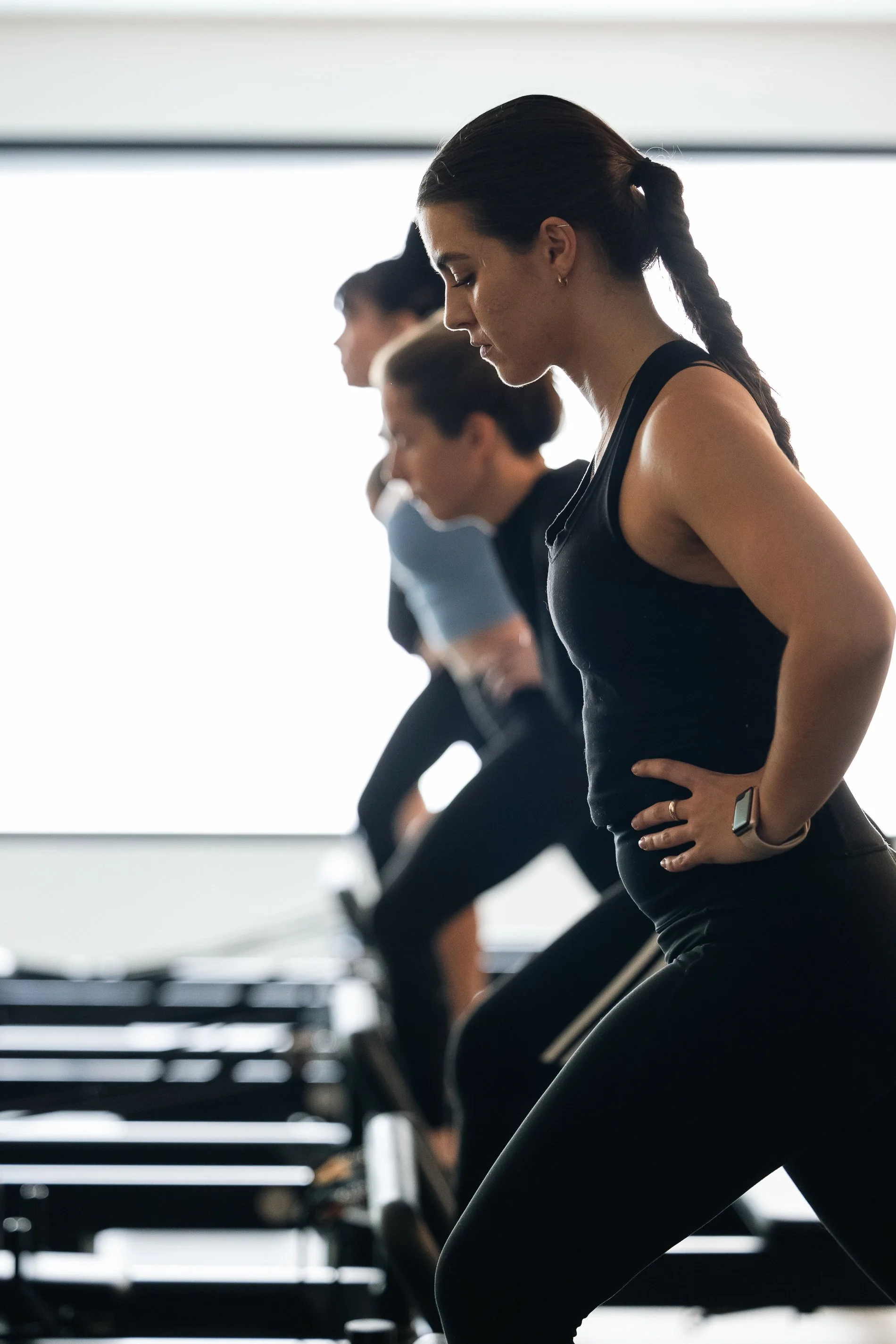 Women doing stretching exercises in a gym with large windows in the background.