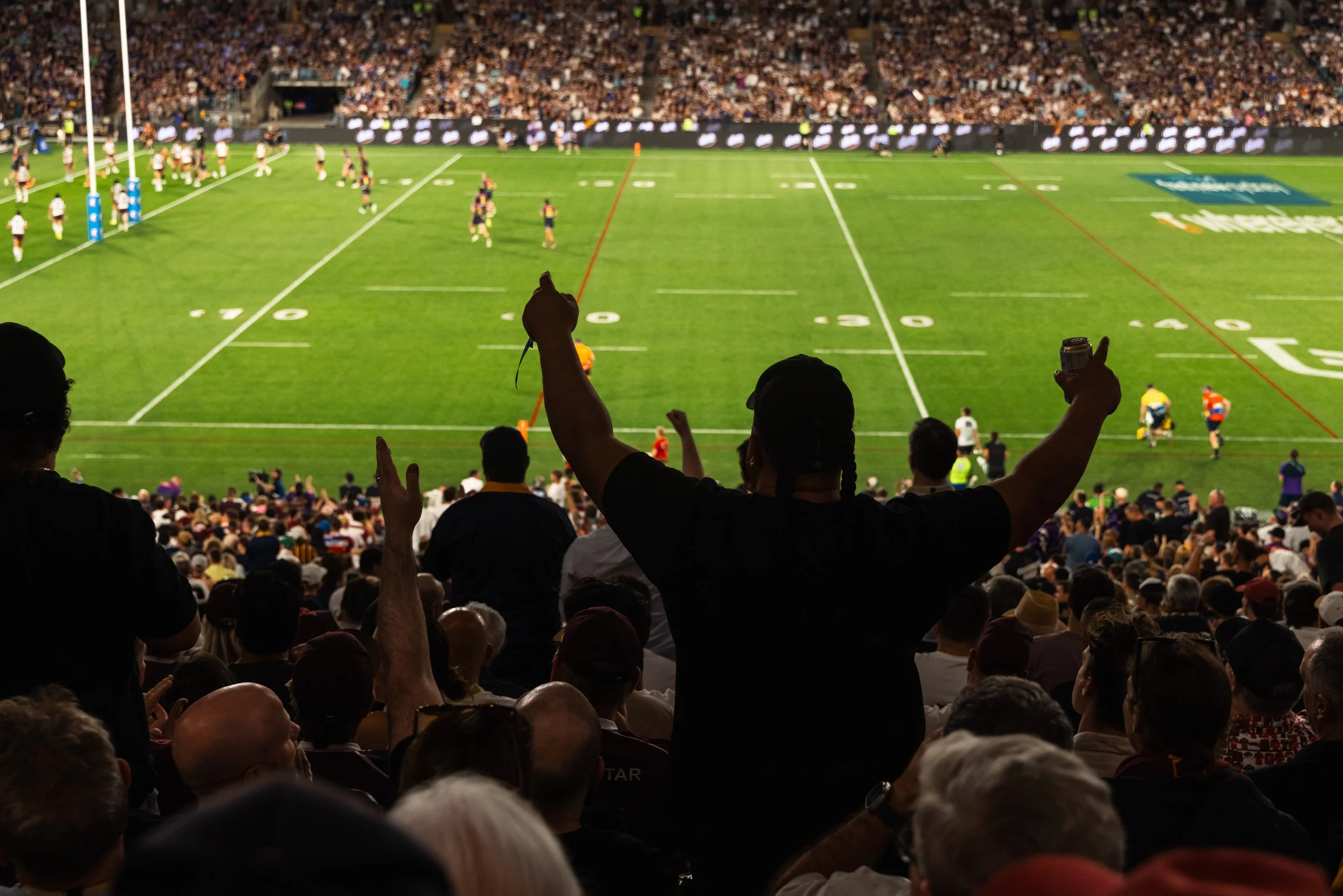 Crowd at a stadium watching a rugby game on the field, with some fans cheering.