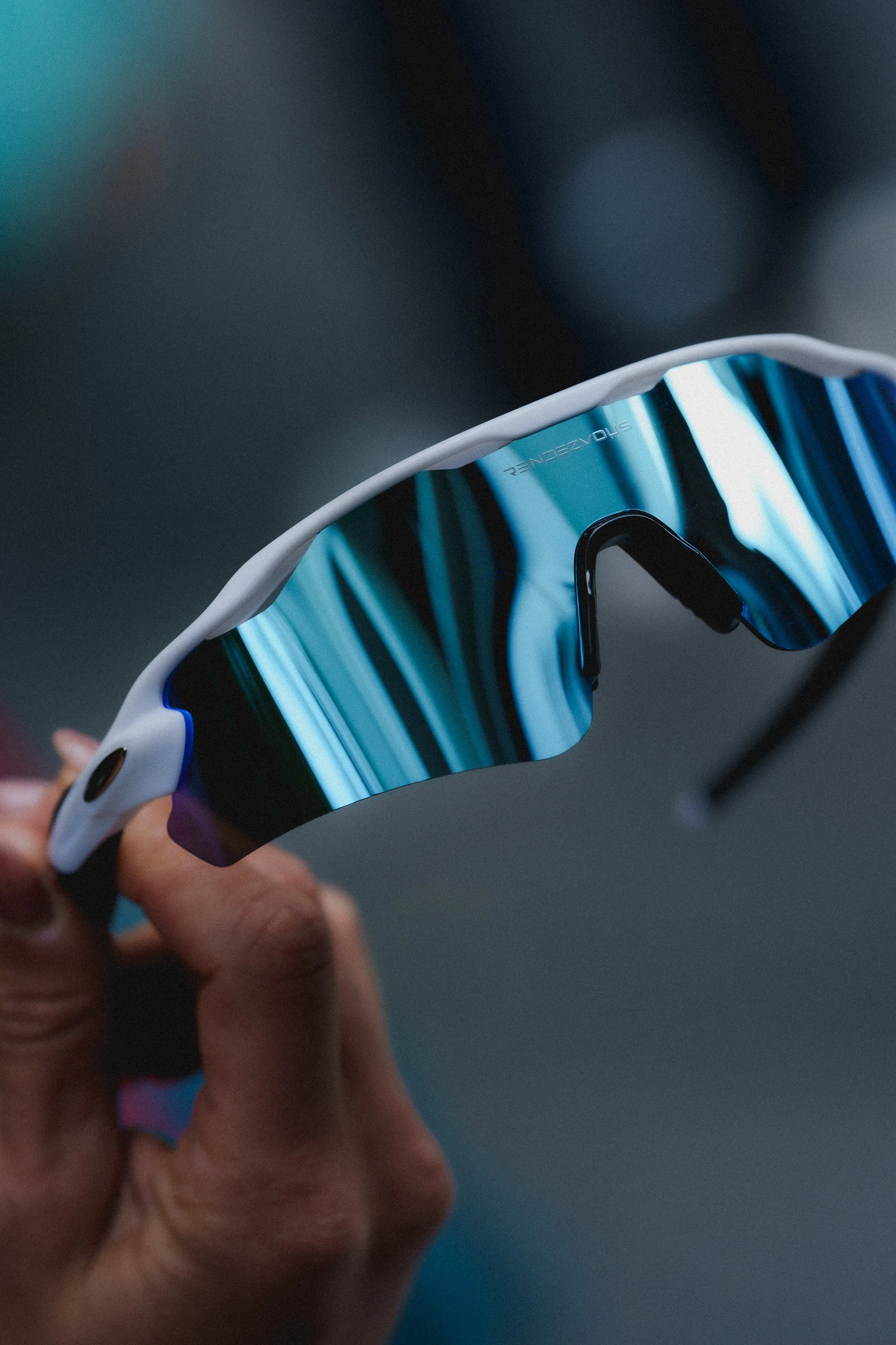 Close-up of a person holding a high-tech sports eyewear with a sleek blue reflective lens.