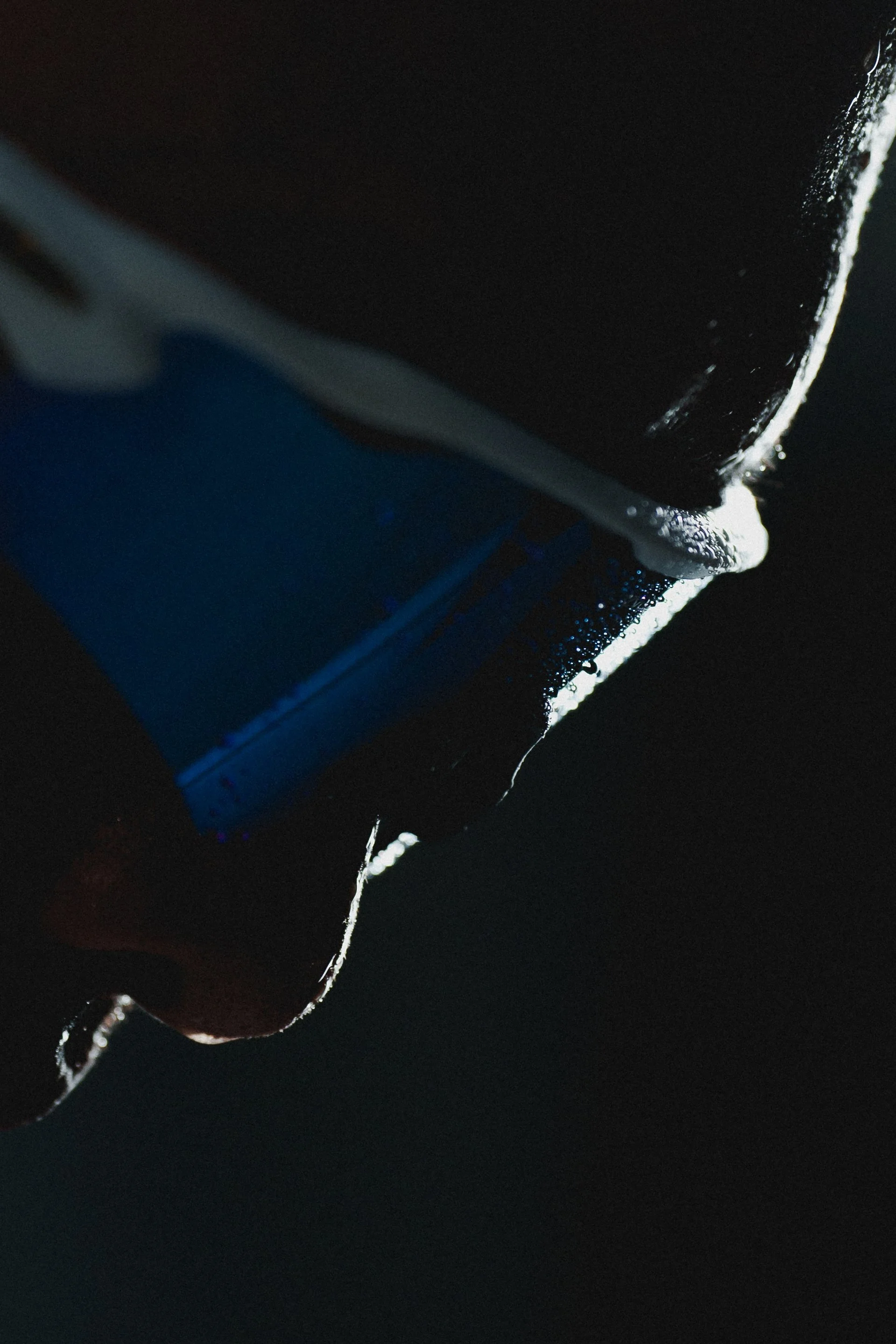 Close-up of a person's hand holding a razer blade, with water droplets on their fingers and black background.