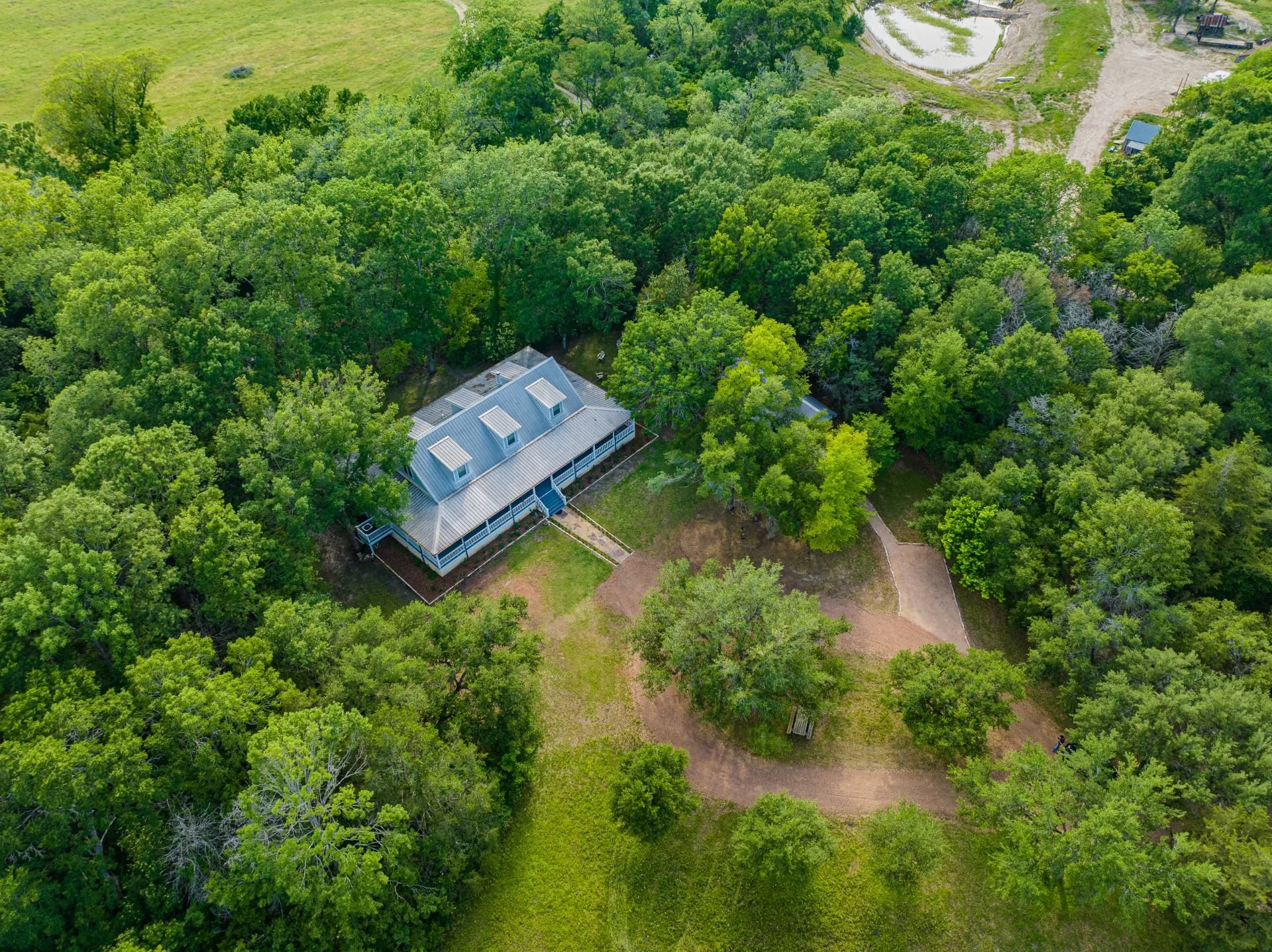 An aerial view of a house surrounded by trees with a yard and walking paths.
