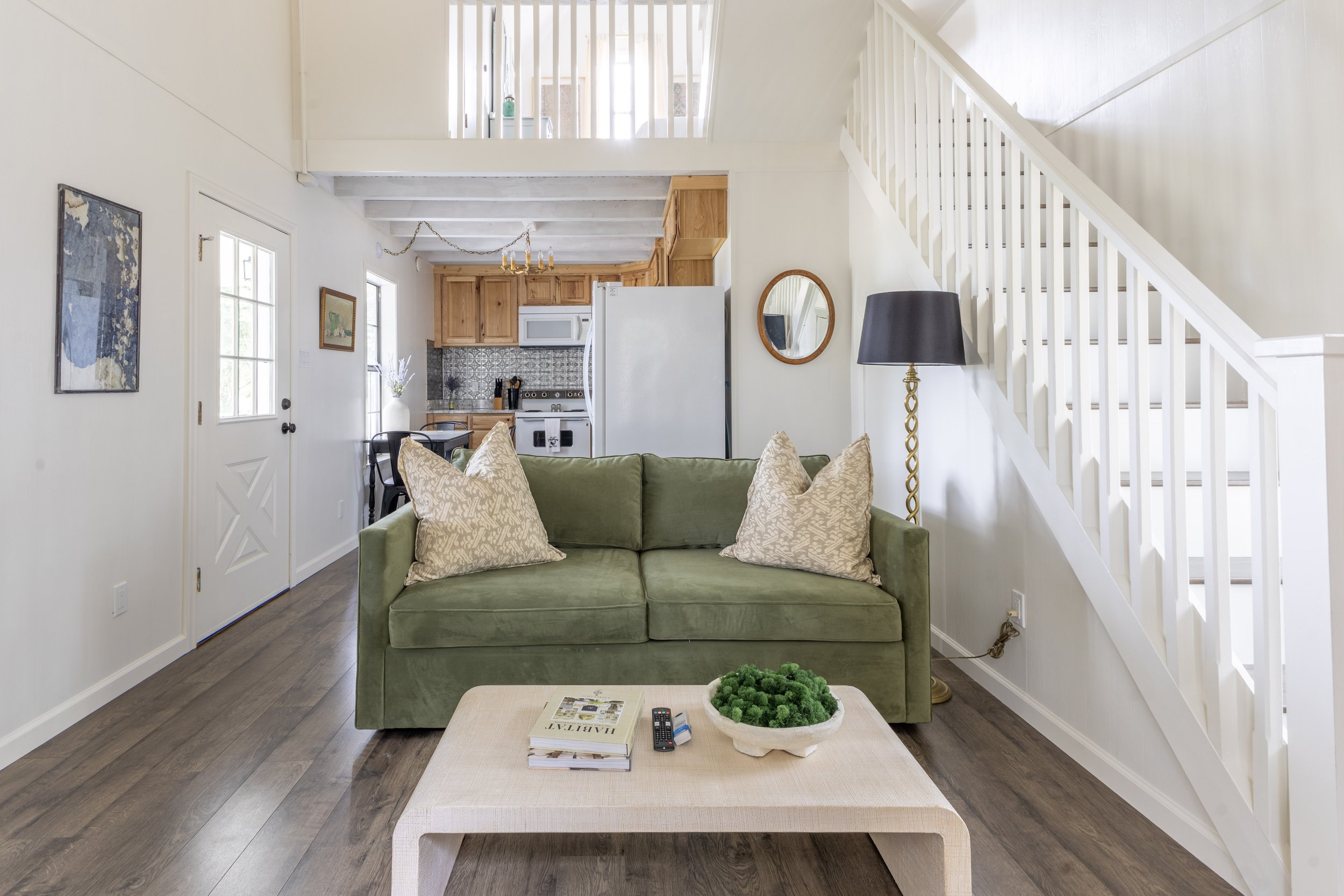 A green sofa and open concept kitchen and living area at The Reed cottage at the Round Top Motel in Round Top, TX