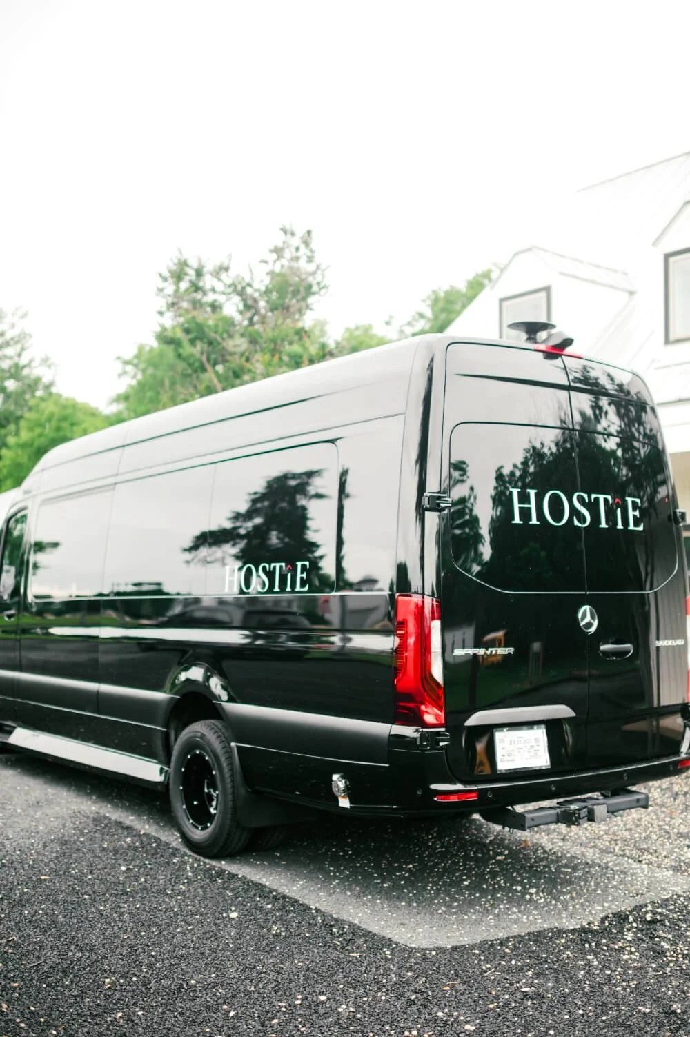 A black Hostie-branded luxury sprinter van parked in front of a house.