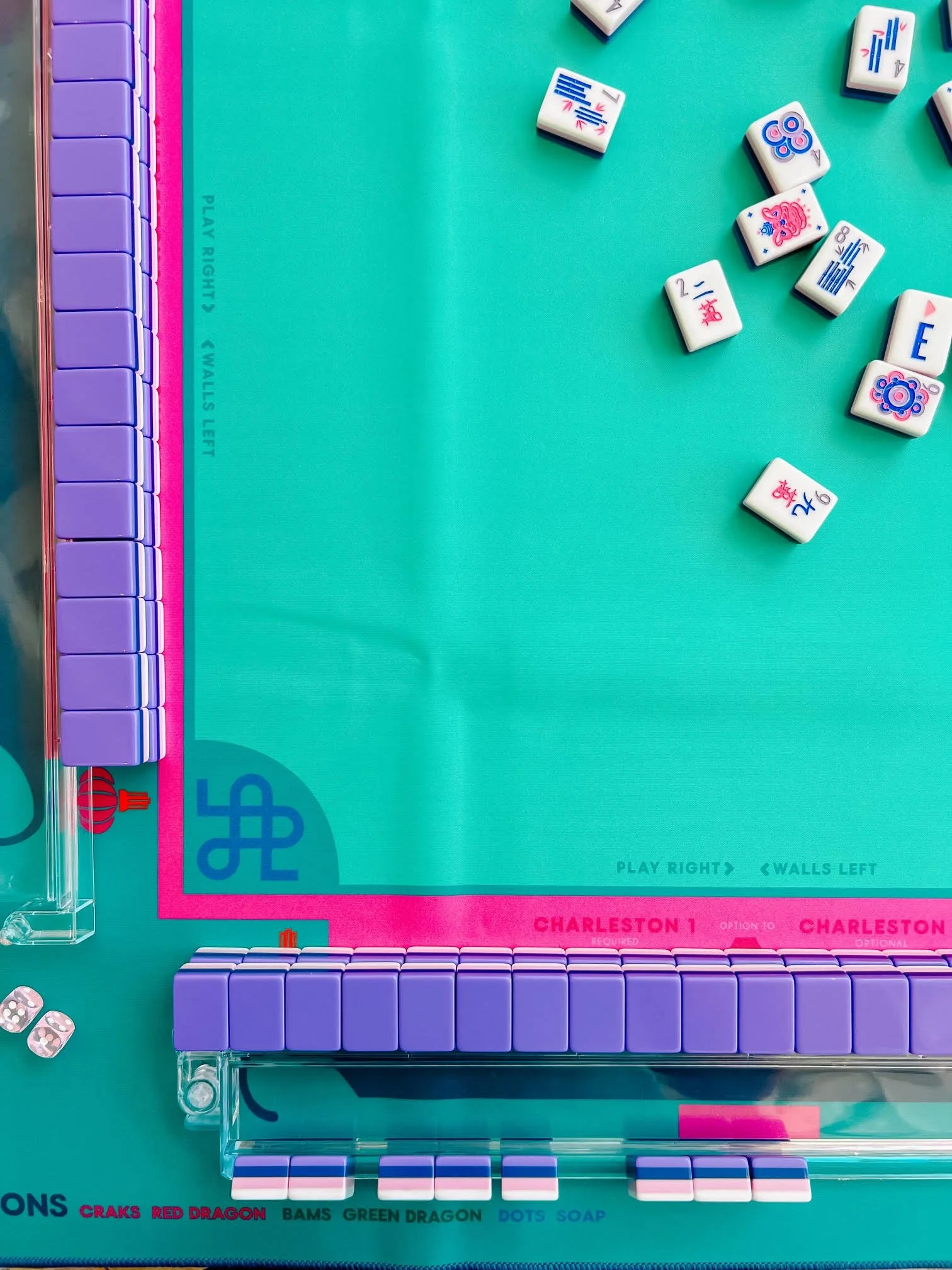 A Mahjong game in progress with a green mat, tiles scattered in the center, and racks holding purple tiles on two sides.
