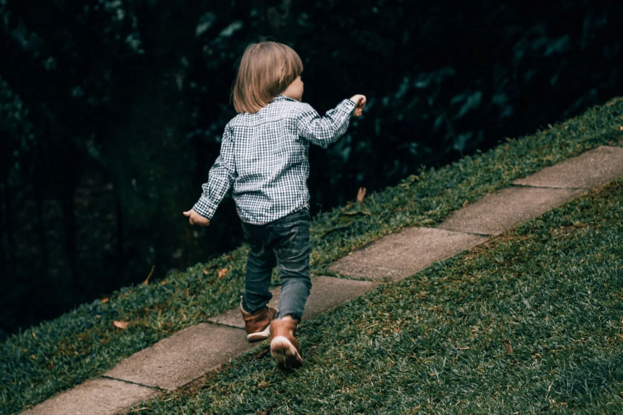 Toddler walking up a grassy slope outdoors
