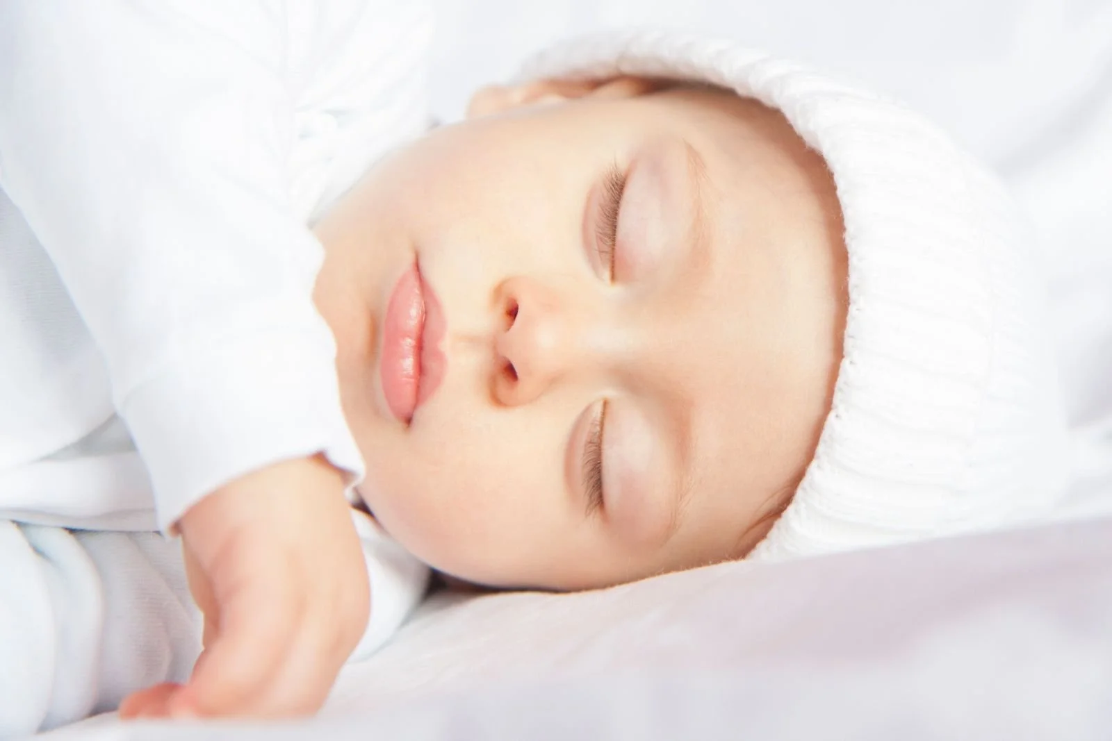 Close-up of a baby in a white knit hat sleeping peacefully with lips closed