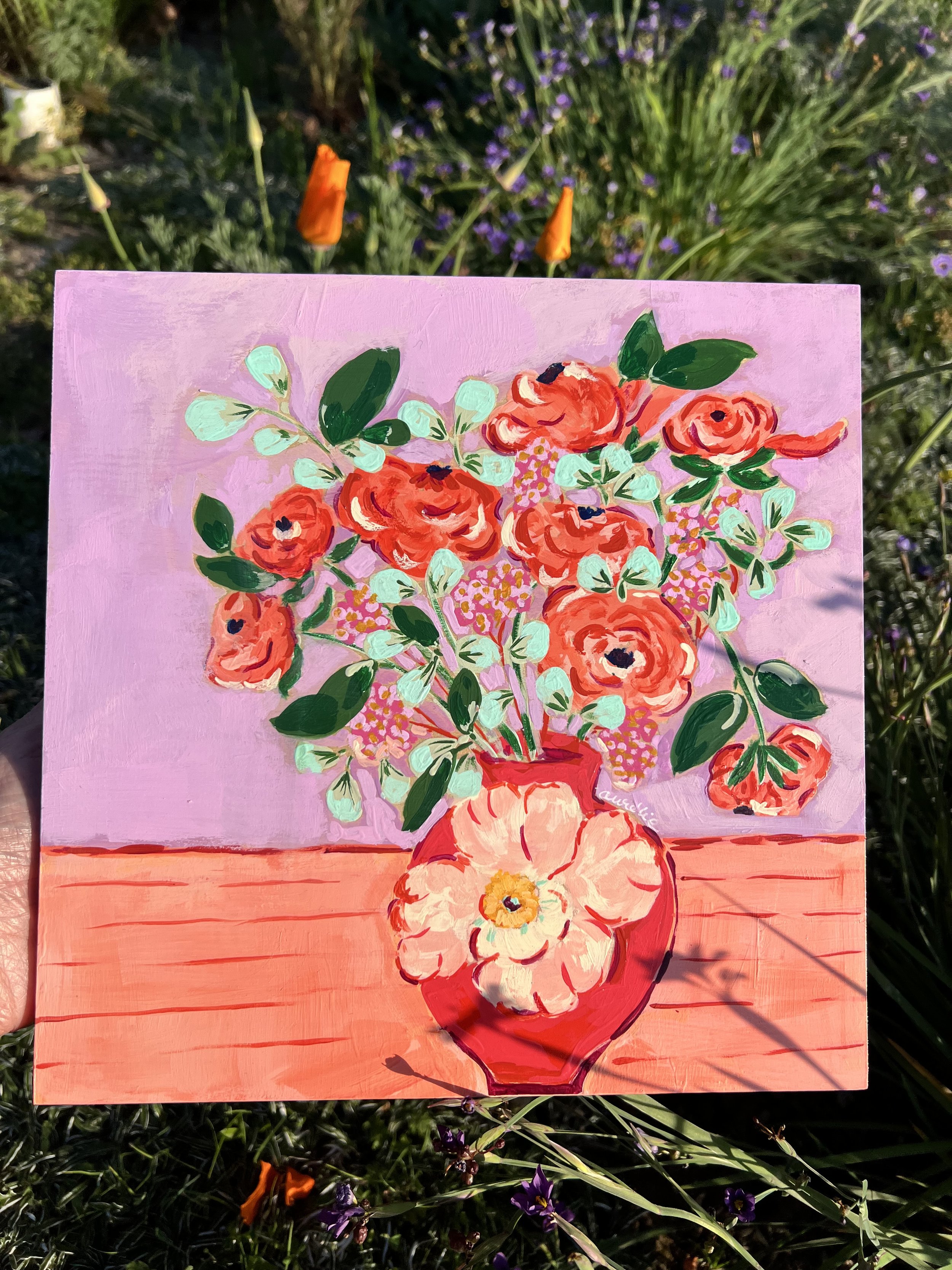 Vibrant orange ranunculus bouquet with mint-green foliage against lavender background. Lovely red vase with its delicate white flower accent. A mix of spring's fresh energy with sophistication.