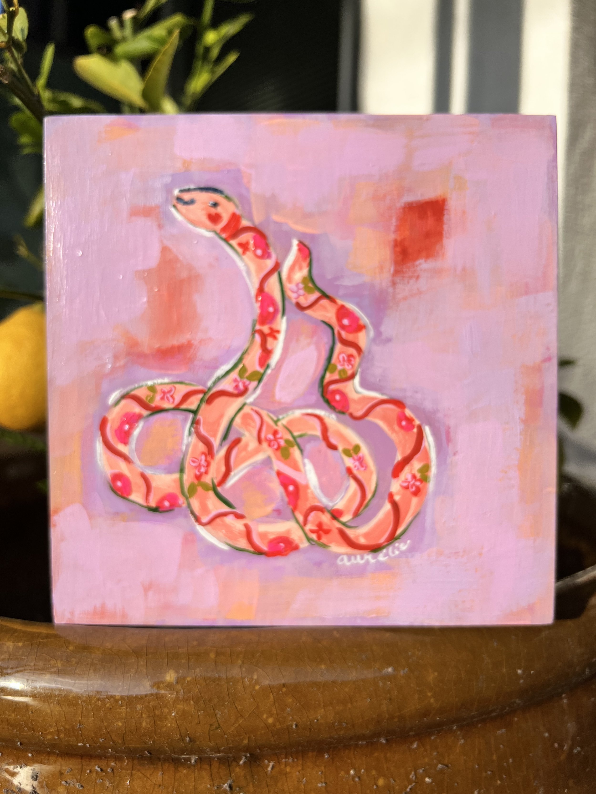 Playful, whimsical, flower-adorned snake that curves against a abstract lavender background. Delicate floral patterns and outlined in crisp white lines, approachable and feminine