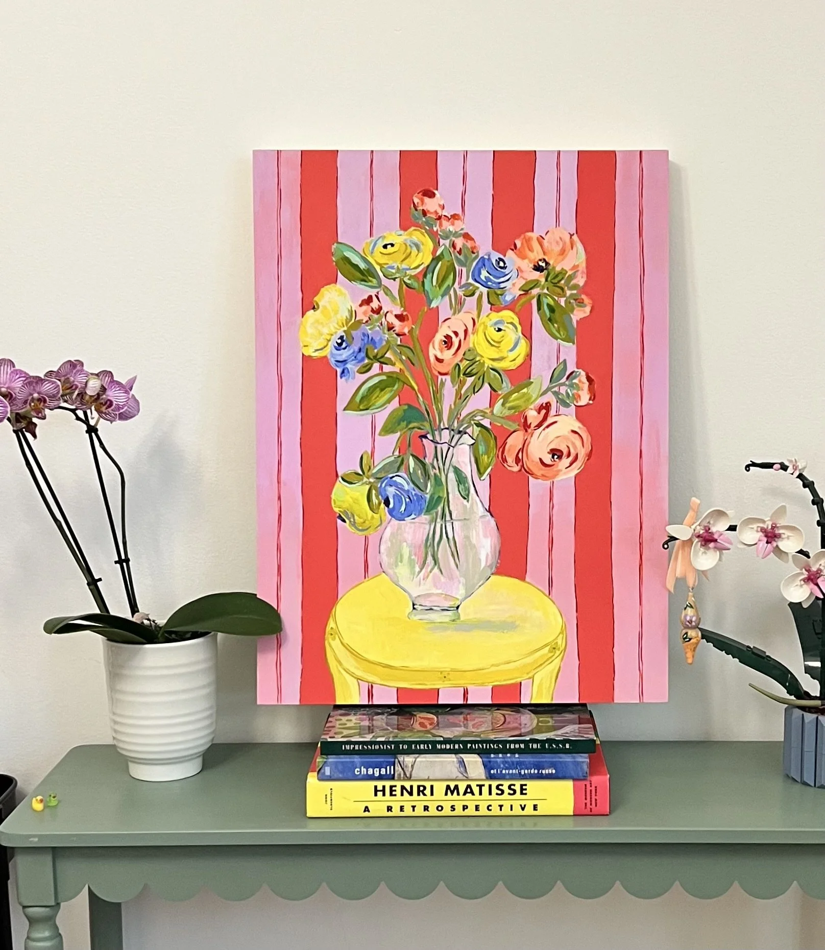 Grand Arrangement of a large bouquet of ranunculus in a transparent vase on bright yellow table. Red and lavender background.