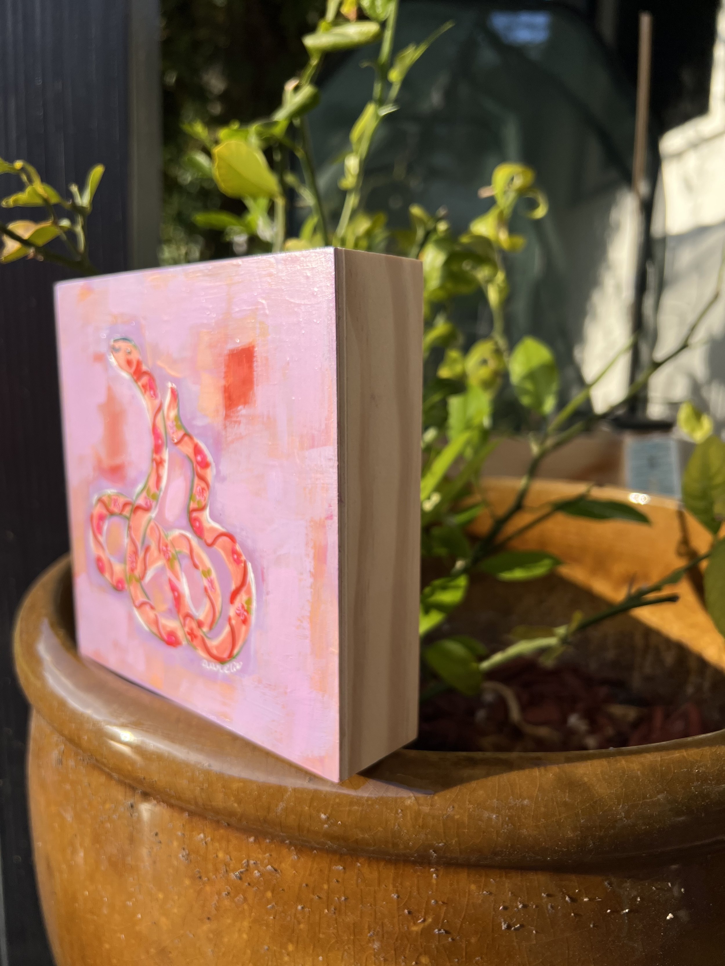 Playful, whimsical, flower-adorned snake that curves against a abstract lavender background. Delicate floral patterns and outlined in crisp white lines, approachable and feminine
