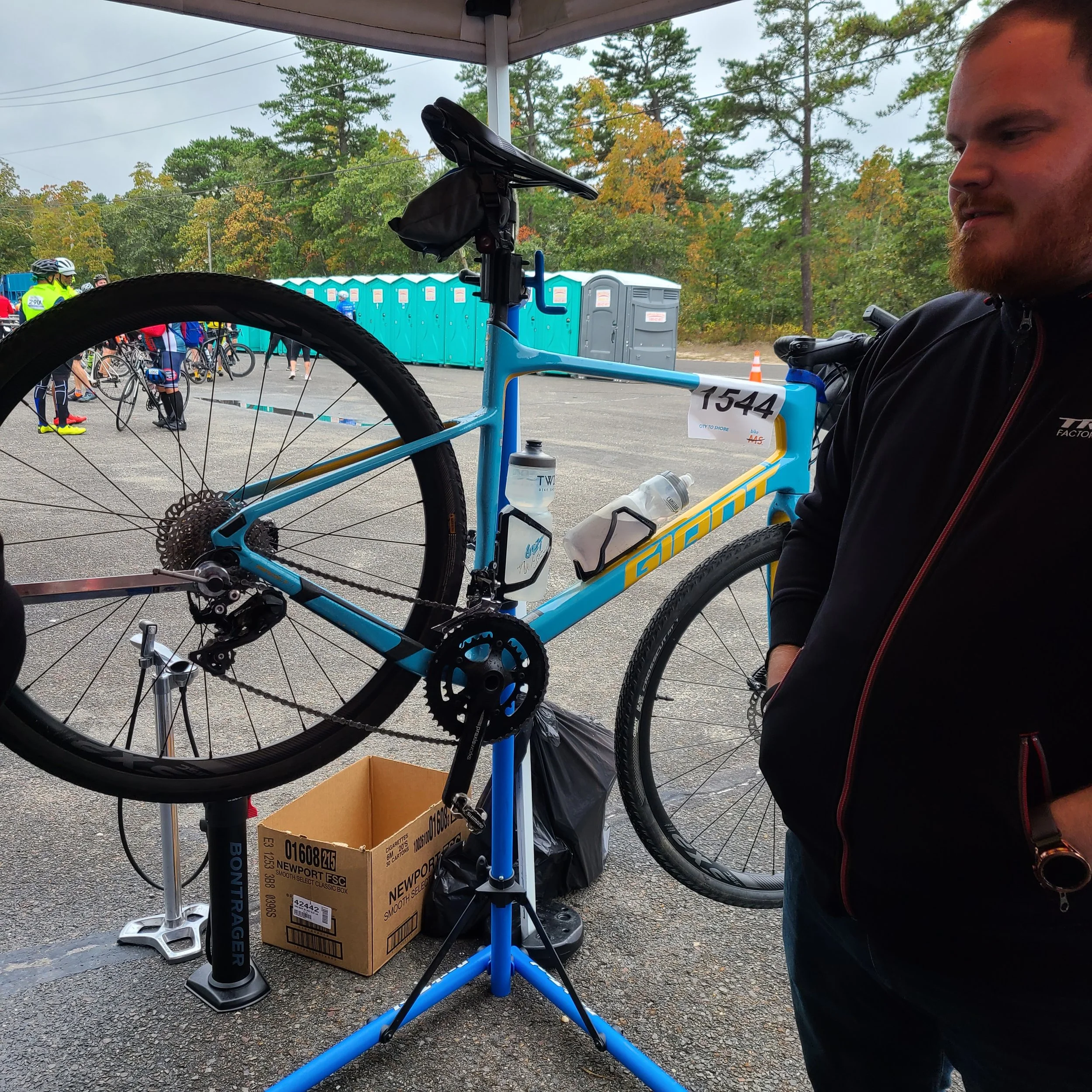 A mechanic stands next to a light blue and yellow Giant gravel bike mounted on a repair stand at an event support tent