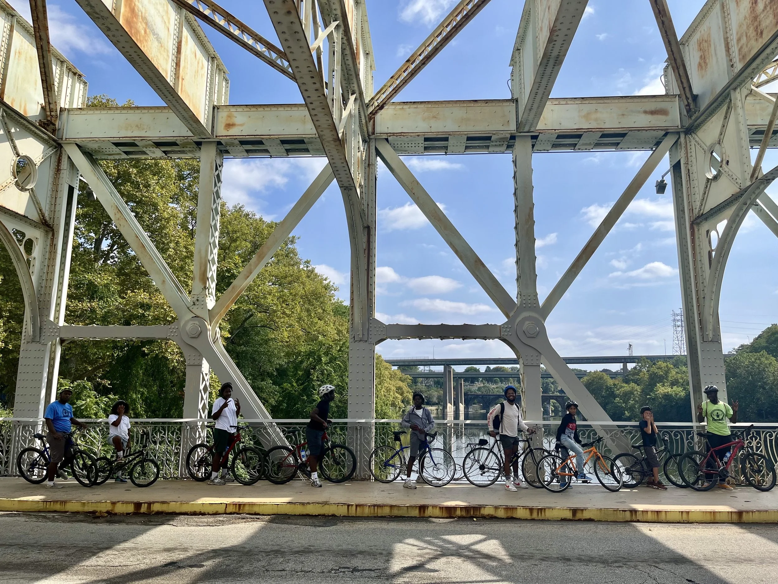 A diverse group of youth and adult cyclists standing with their bicycles on the East Falls Bridge in Philadelphia for Bike Month.