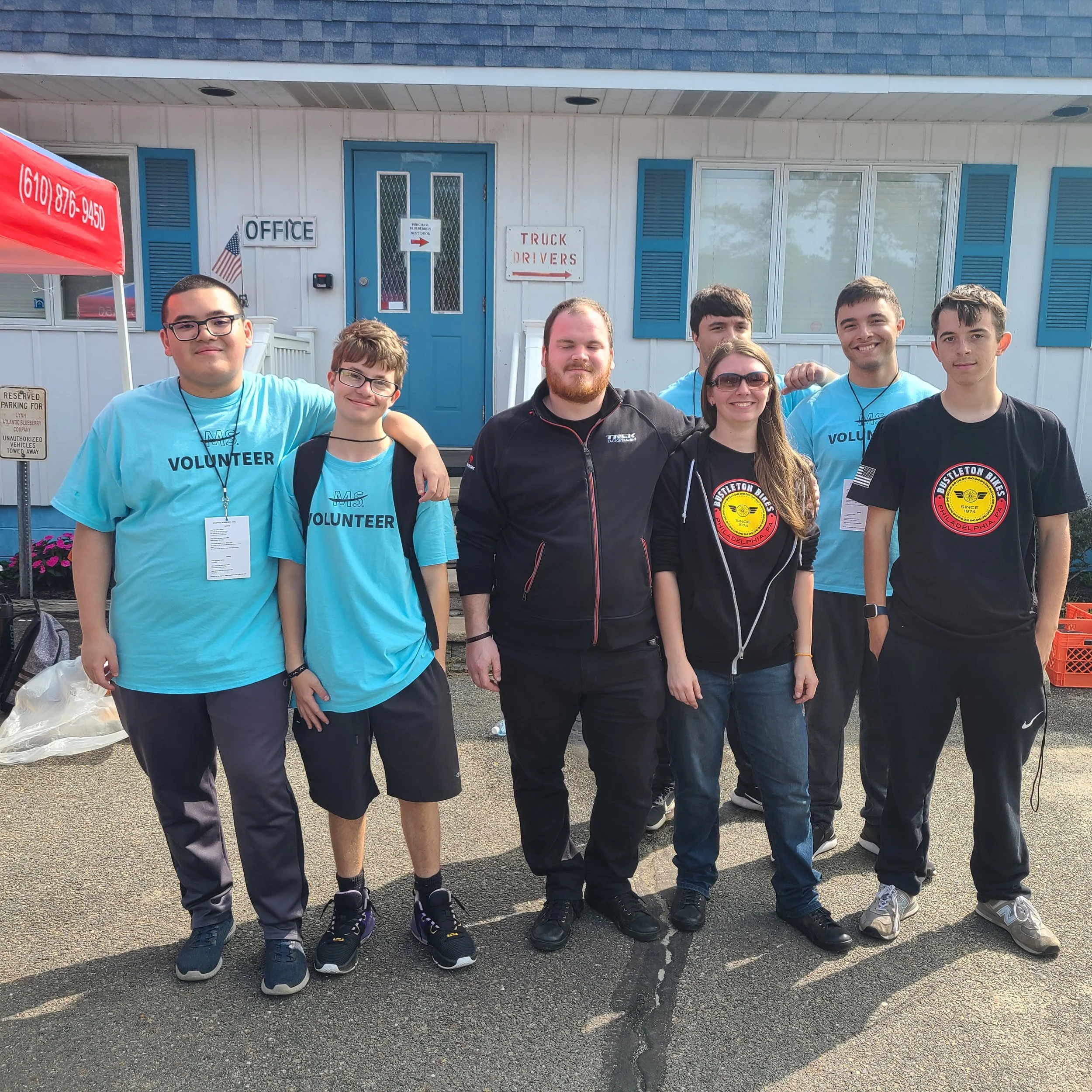 Two bike shop mechanics alongside volunteers from a local Philadelphia school at the MS Bike Ride, posing together outdoors.