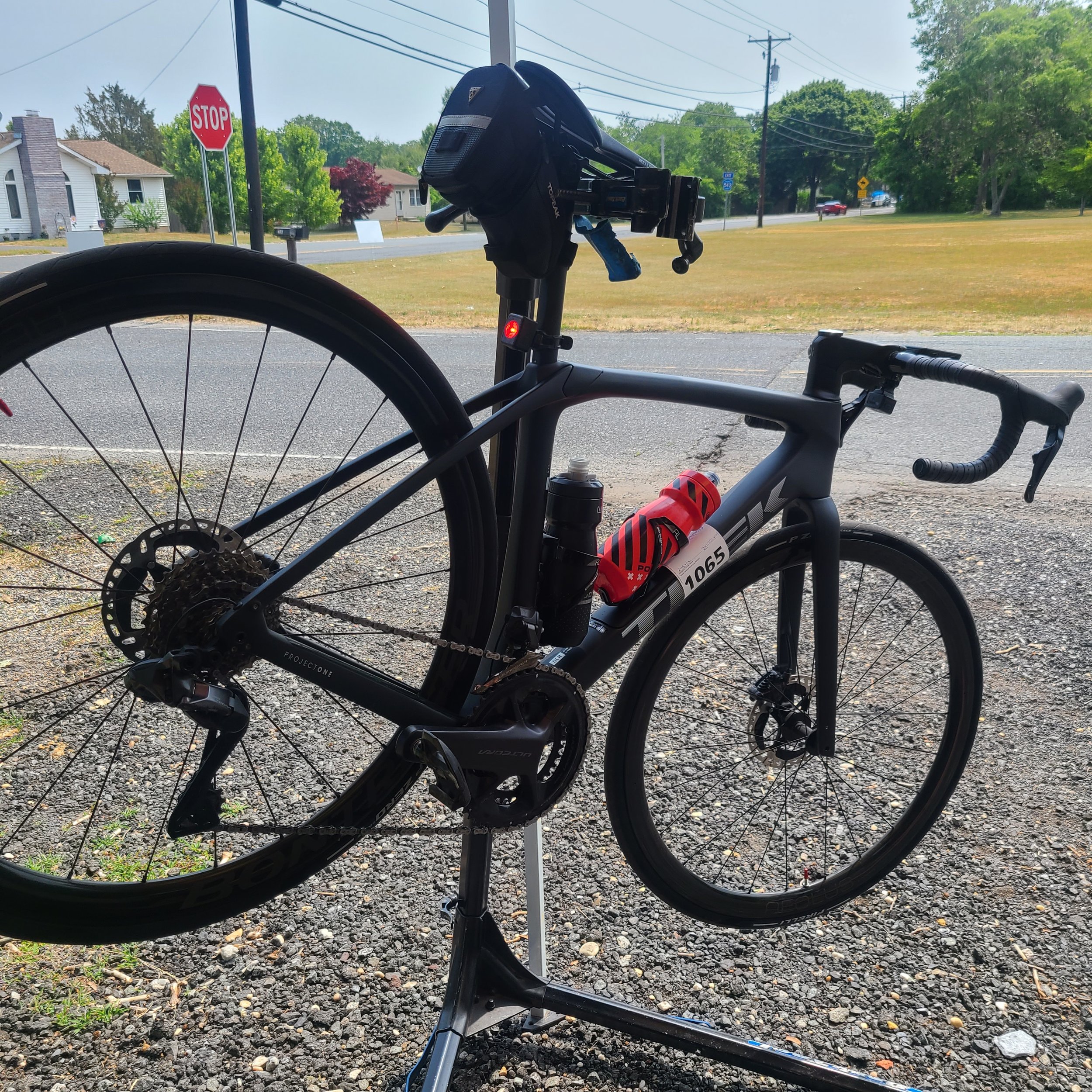 A mechanic's hands adjusting the drivetrain of a bicycle clamped into a heavy-duty portable work stand at an outdoor charity ride event.