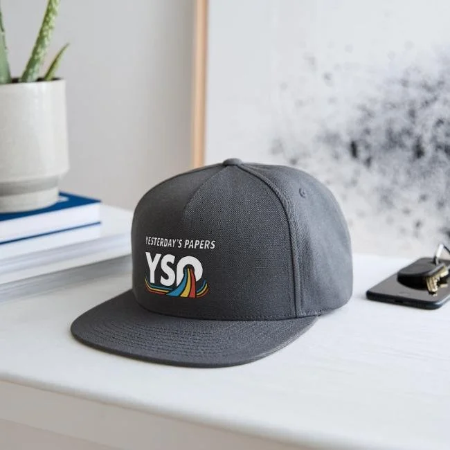 Dark grey snapback flat-brim hat featuring the official white and retro color ribbon logo for 90s alternative cover band Yesterdays Papers designed by Sketch Simply.