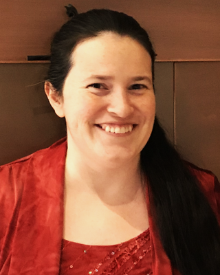 A woman with dark hair smiling in a red top, sitting indoors.