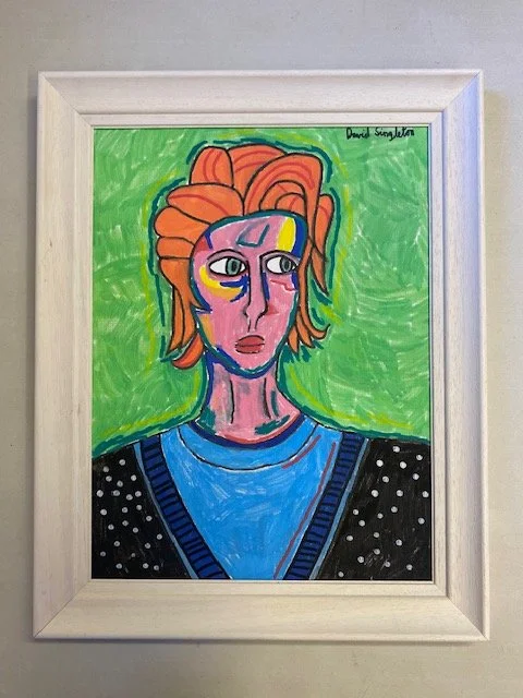 Colorful abstract painting of a person with orange hair, pink face, and green eyes, lying on a blue surface with a starry black background and a green background.. Painting is in a white frame