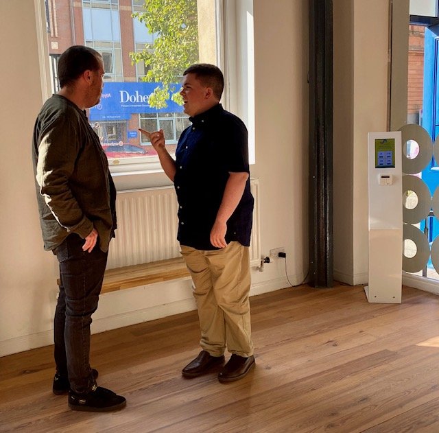 Artists David Singleton and Michael Hade talking in front of a window in the Atypical Gallery