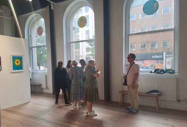A group of people looking at the artwork in the Atypical Gallery. They have large curved windows behind them.