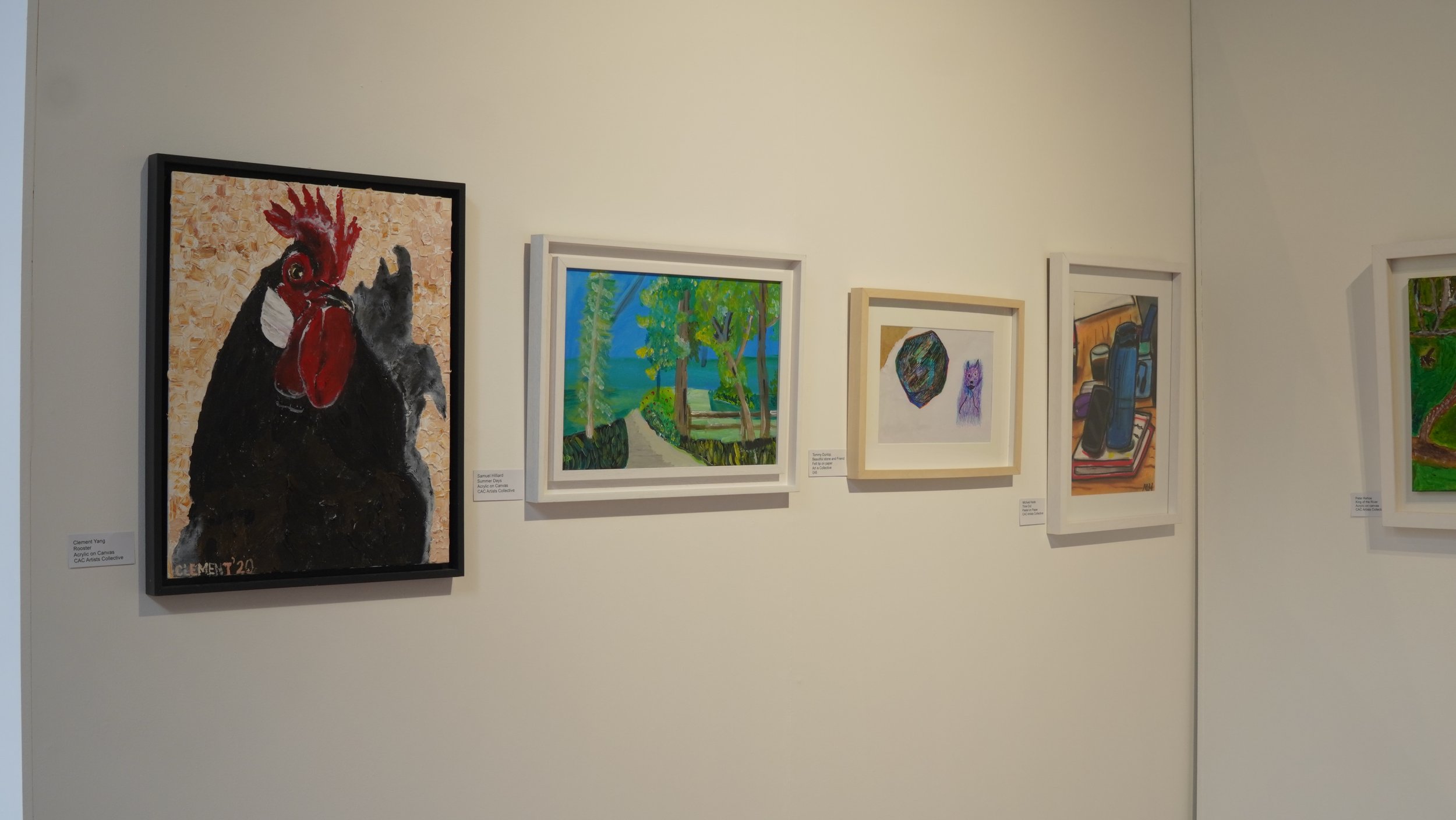 A black rooster painting with a red comb and wattle hangs on a white wall in an art gallery, alongside other framed artworks.