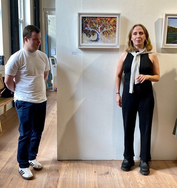 Artist Joe Hallam and Mags Salisbury in front of his artwork "the four seasons" hanging in the Atypical Gallery