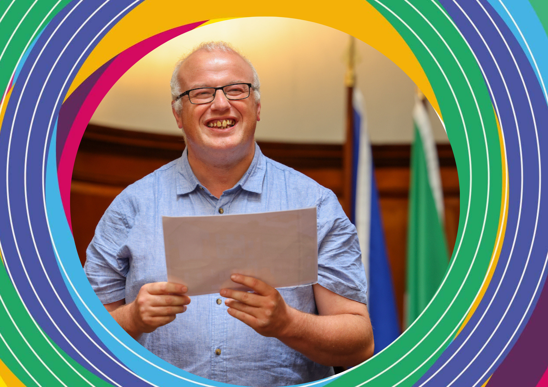 Artist Alan Tarpey, a bald man with glases wearing a powder blue shirt, holds a horizontal sheet of paper.