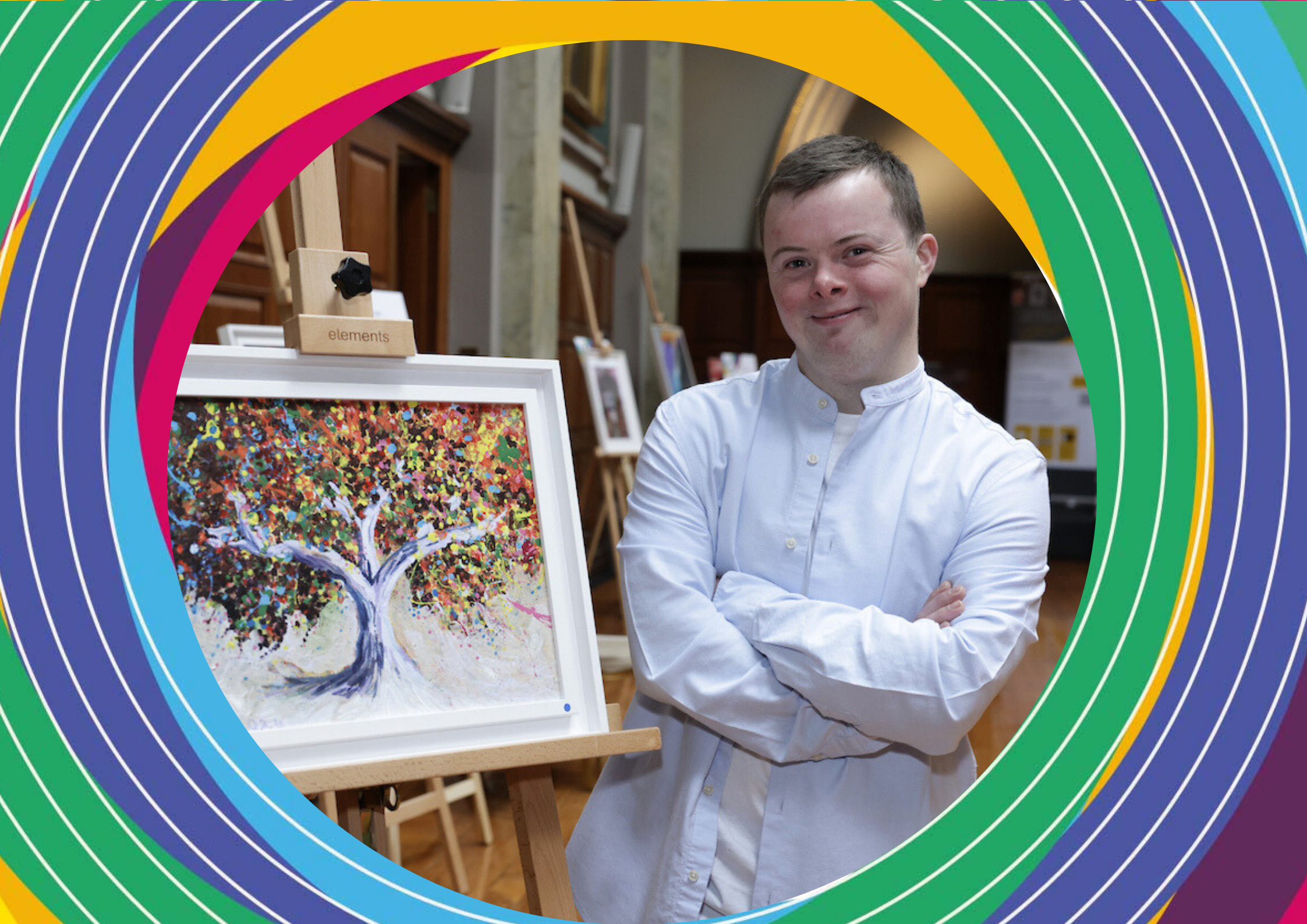 Artist Joe Hallam, wearing a white shirt, stands next to his pointillist painting of a tree