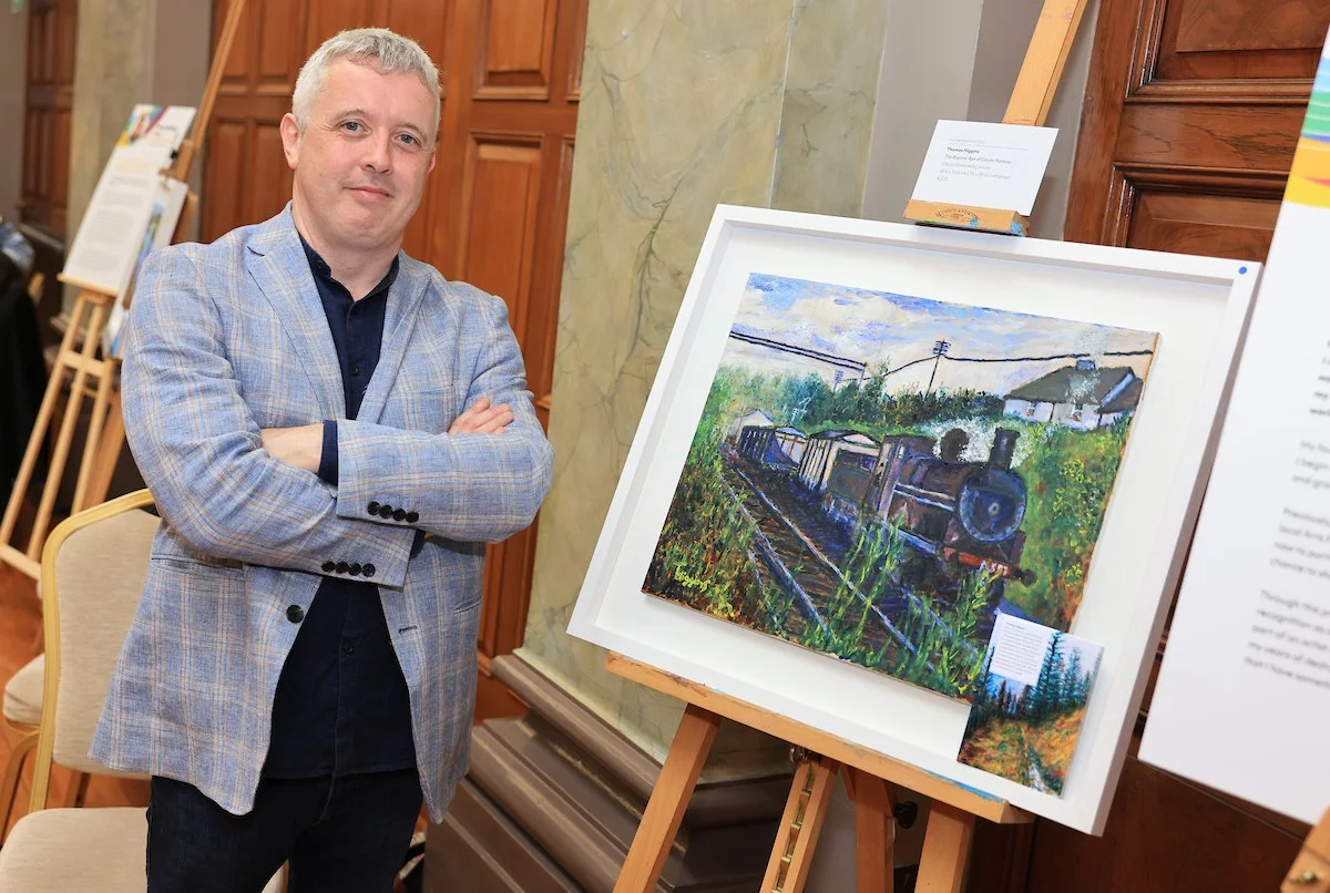 Artist Thomas Higgins in a plaid jacket next his painting of a train