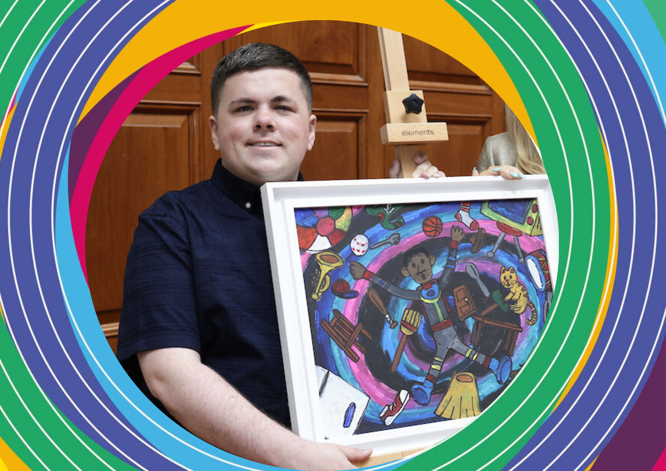 Artist Michael Hade, a man wearing a dark blue shirt, holds his white framed artwork of an abstract form in front of him.