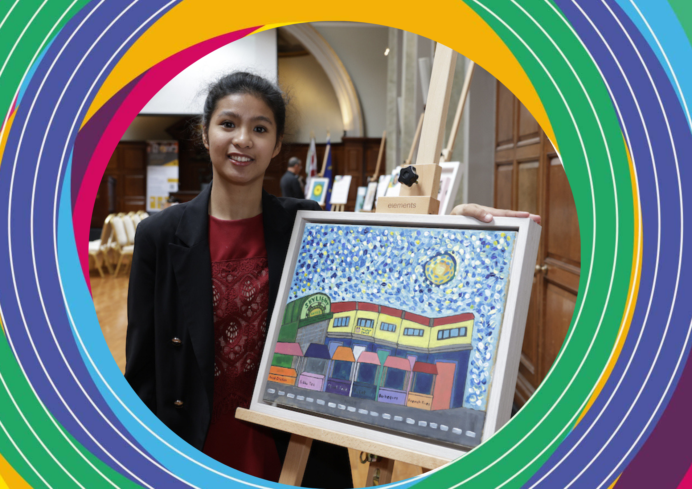 Artist Kristin Reynado Suniga, an Asian woman with tied back dark hair, stands next to her artwork on an easel of a street in Santiago.