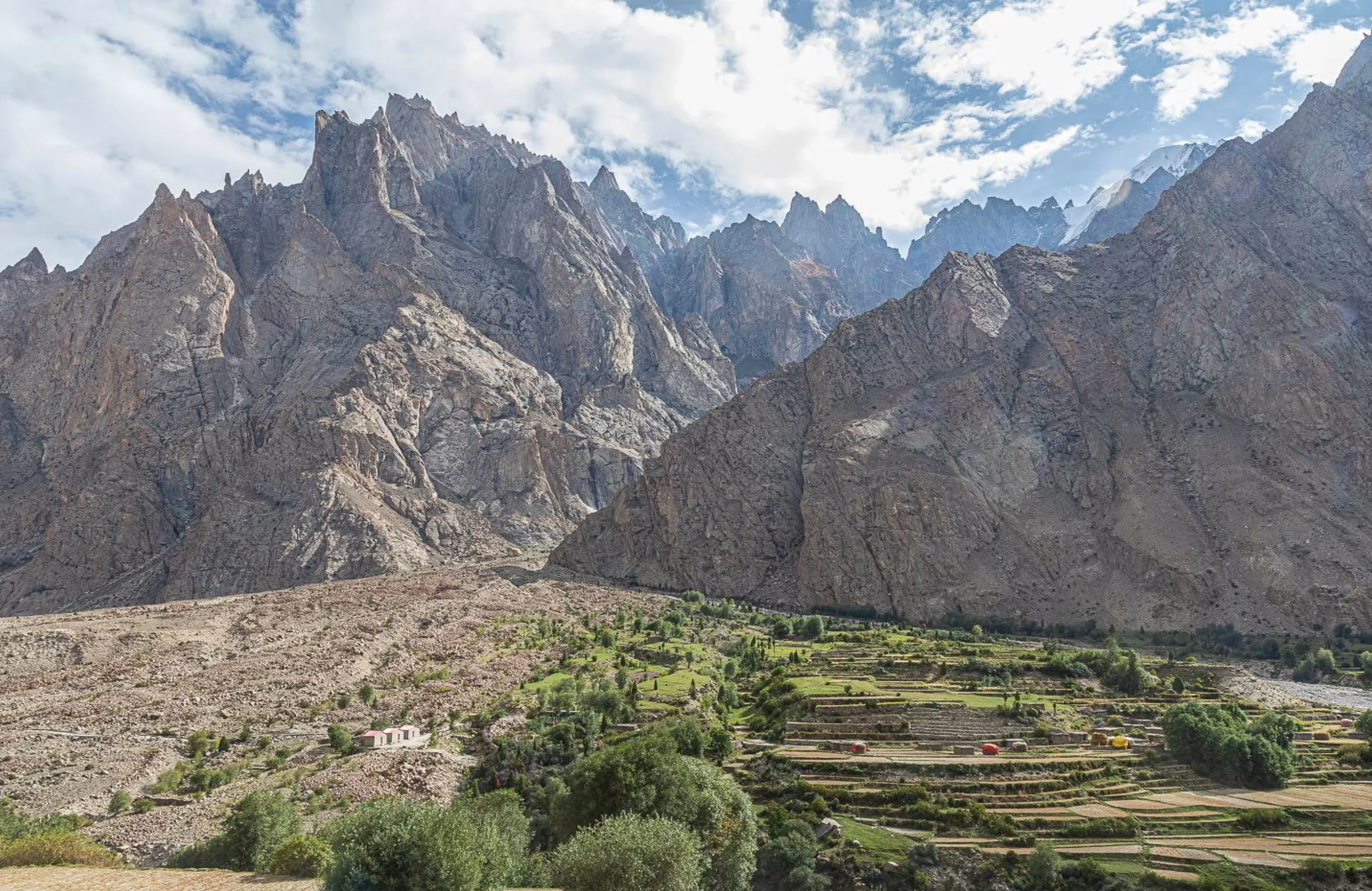 Scenic view of rugged mountain range with steep, jagged peaks and terraced green fields at the mountain's base.