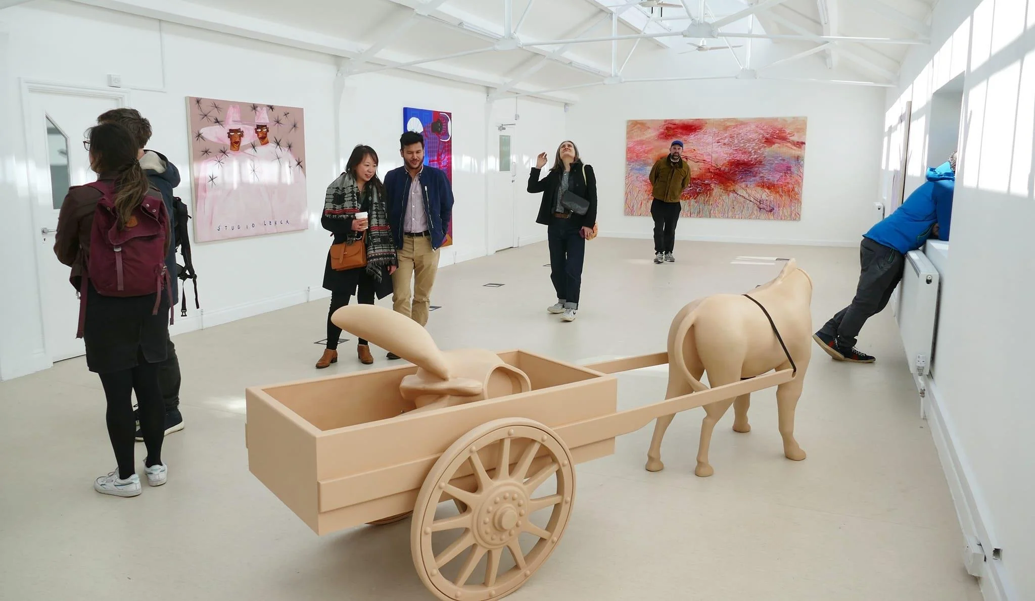 People viewing artwork in an art gallery with a large sculpture of a horse pulling a cart in the foreground.