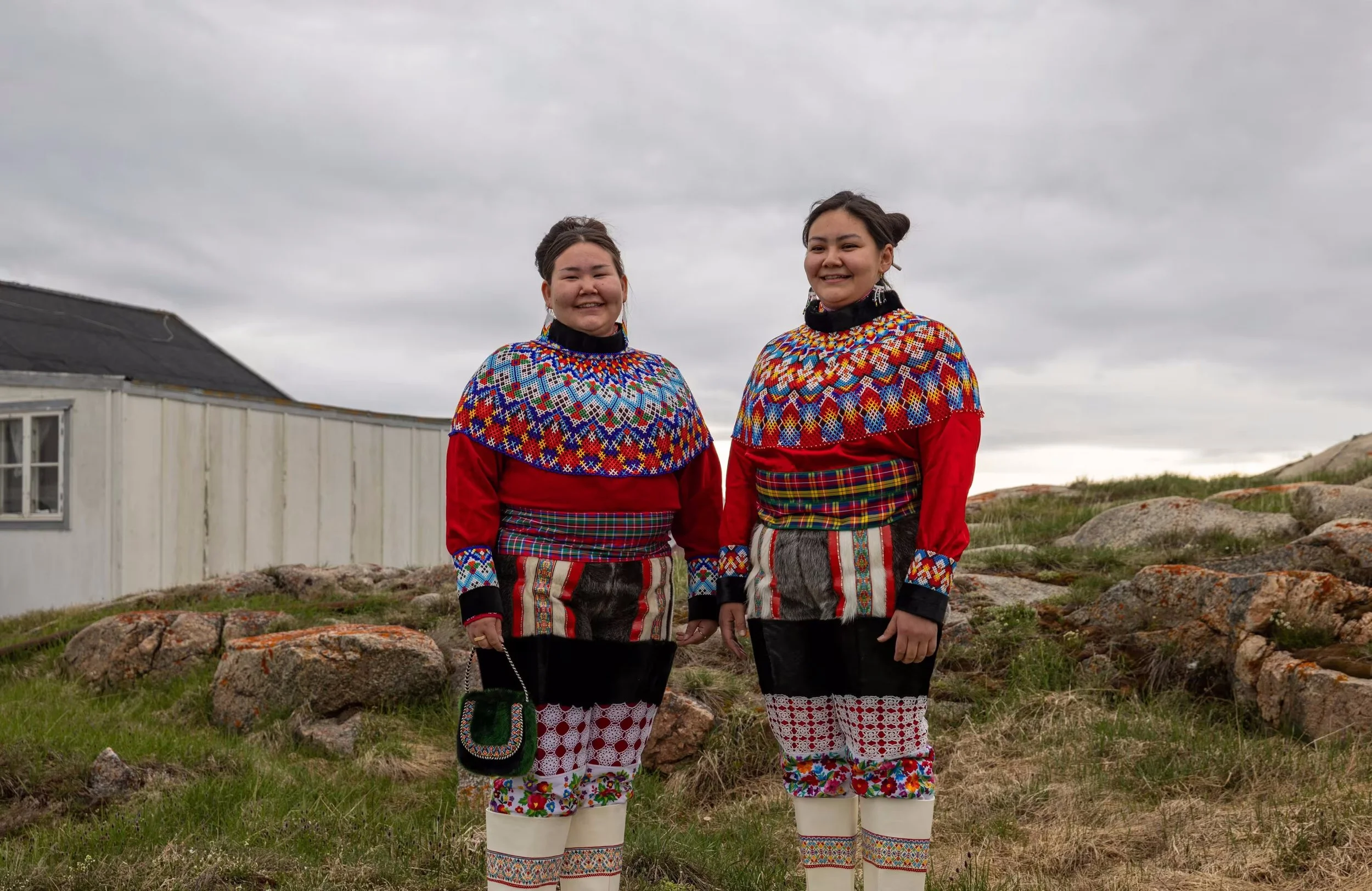Two women wearing traditional, colorful, embroidered clothing and jewelry, standing outdoors on a cloudy day.