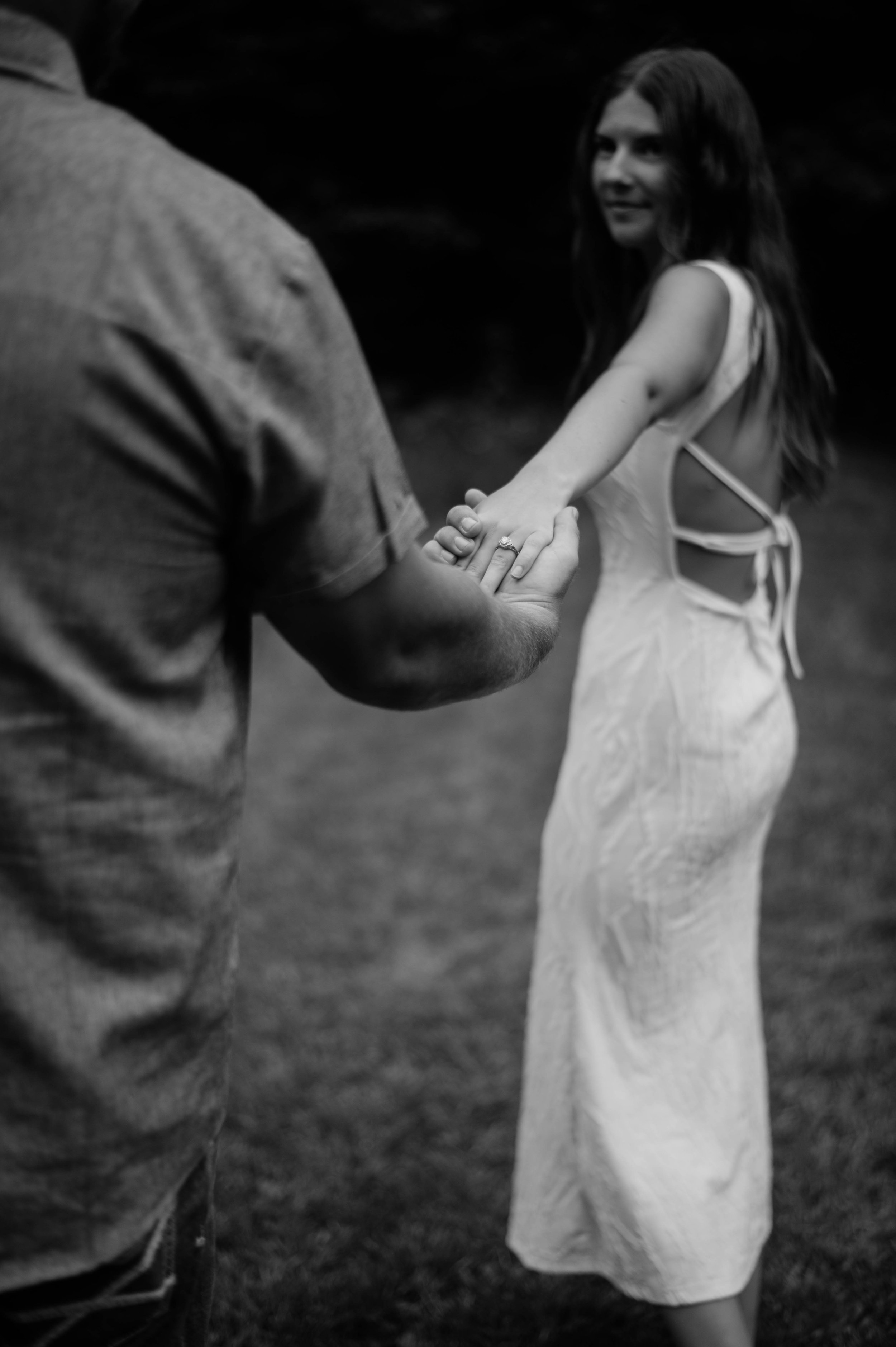 engaged couple, woman holds man's hand and leads him on a walk showing her engagement ring