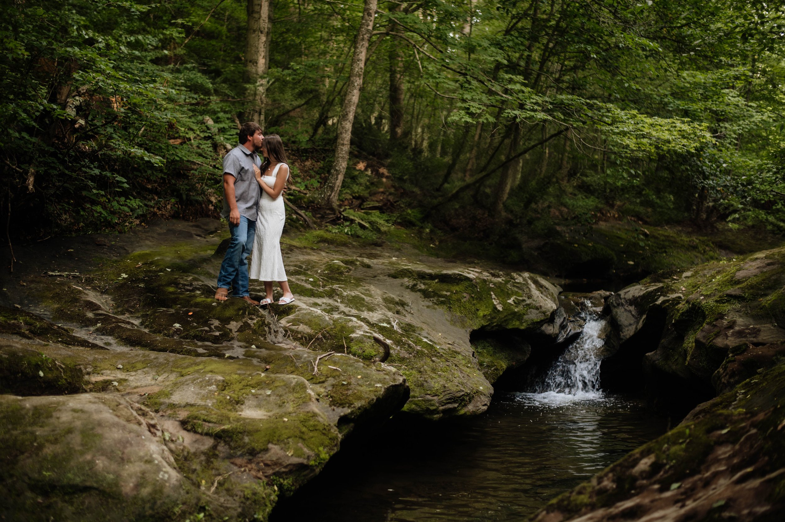 Engaged couple snuggle on a rock near a waterfall