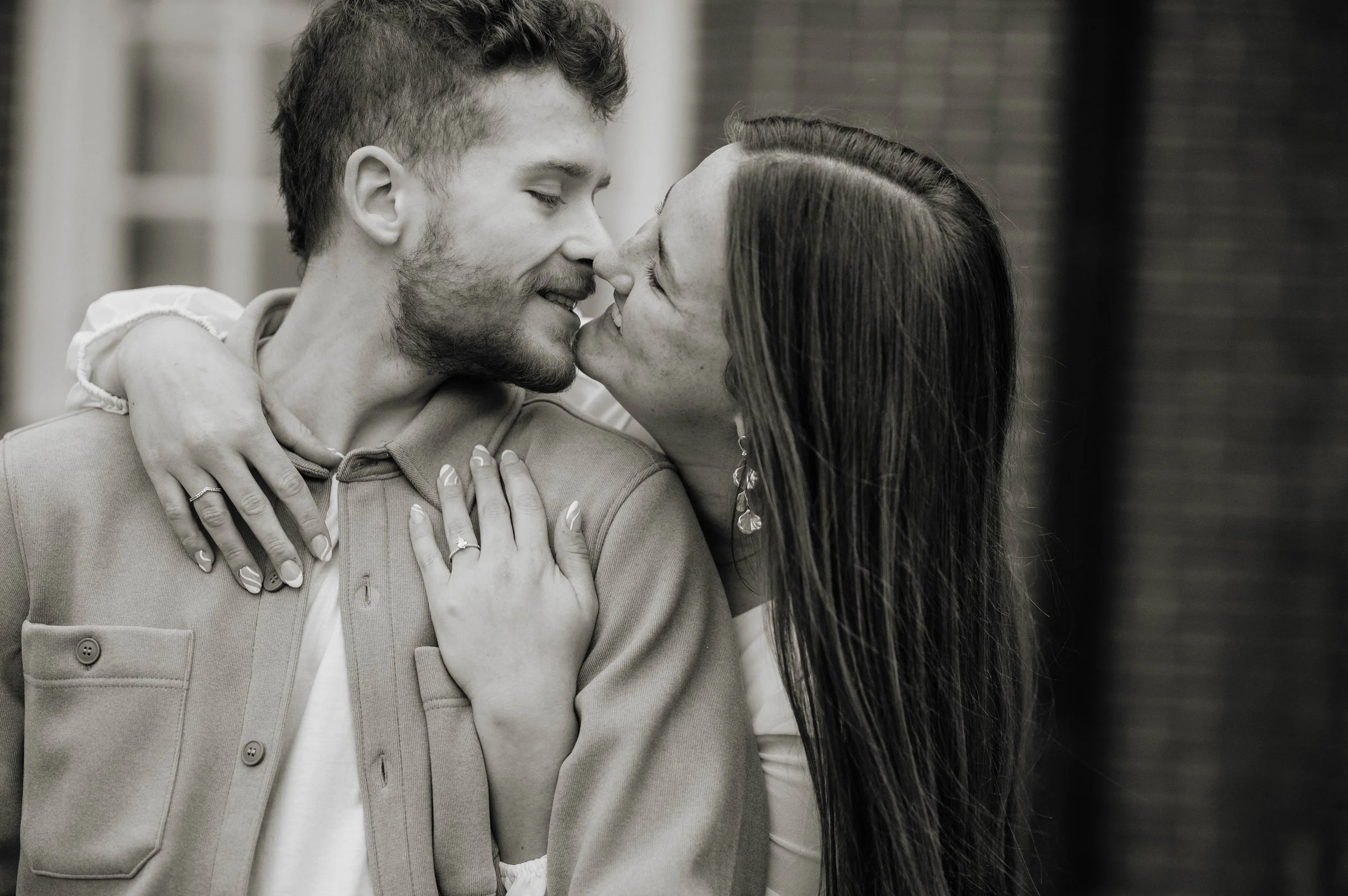 A black and white photo of a couple close together, smiling and about to kiss, with the woman leaning in toward the man.