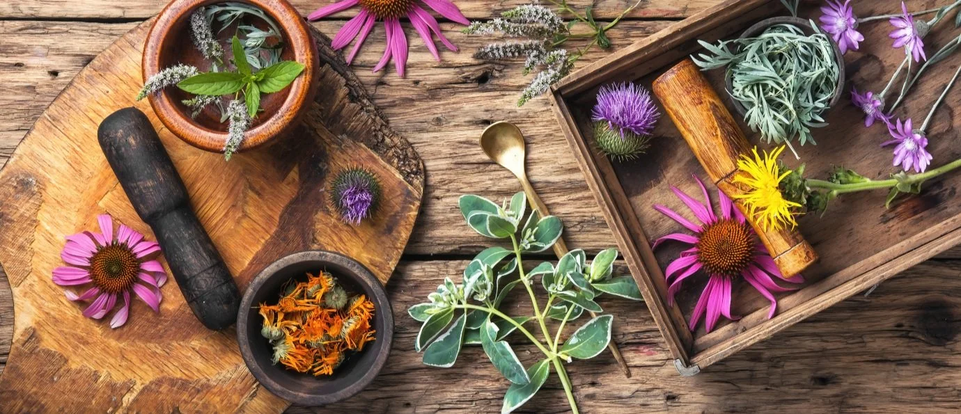Herbs and flowers on wooden table with mortar and pestle.