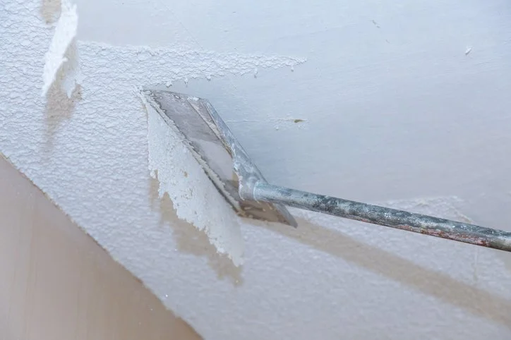 Close-up of a drywall repair process with a putty knife applying joint compound to a textured wall surface.