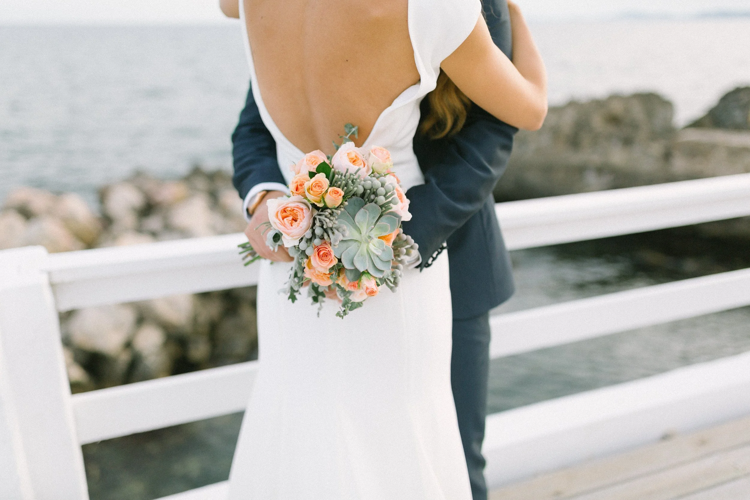 Pareja en boda en la playa, con la mujer sosteniendo un ramo de flores color durazno y verde.