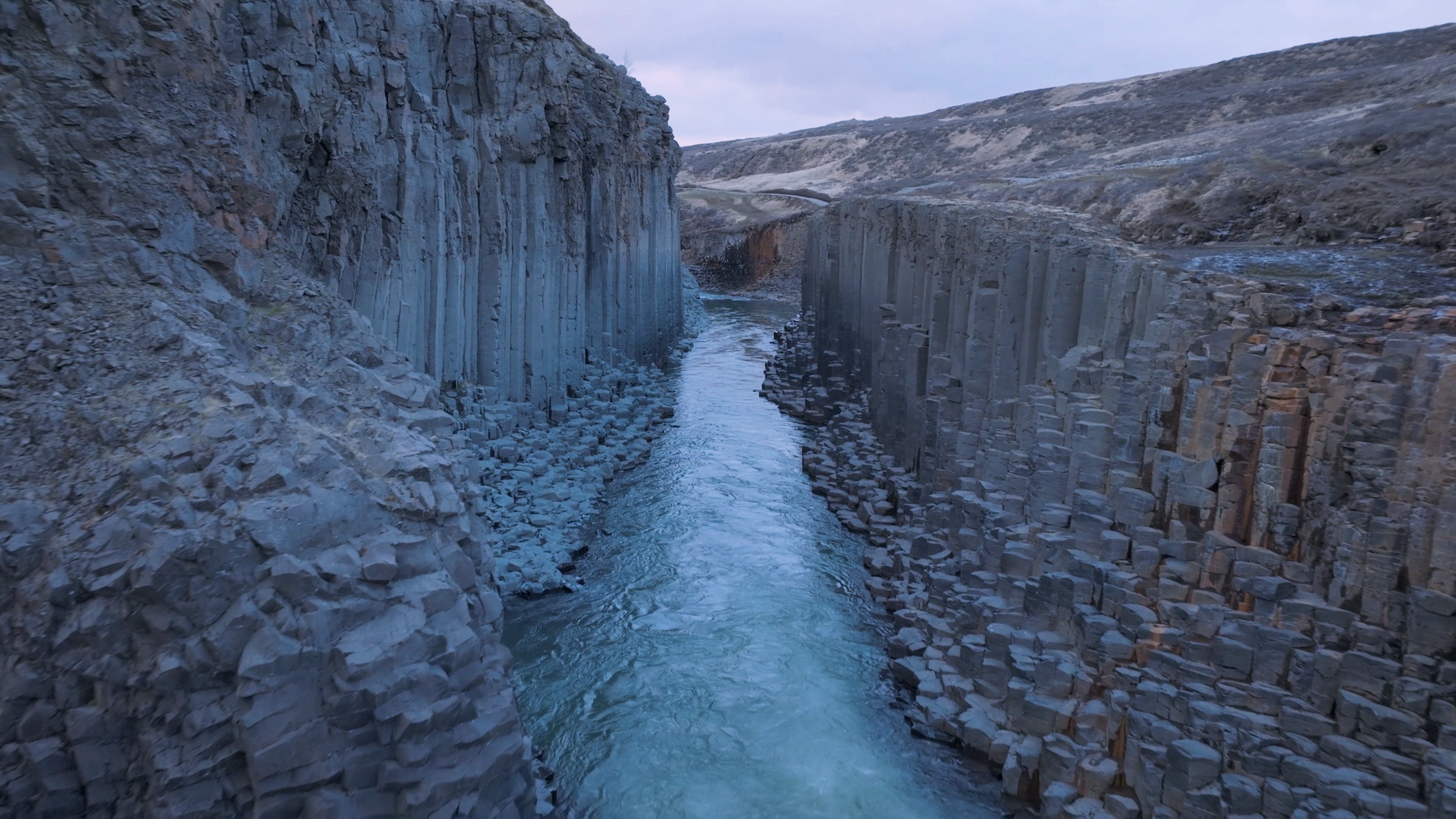 A narrow canyon with tall, vertical rock cliffs on each side and a river flowing through the bottom.