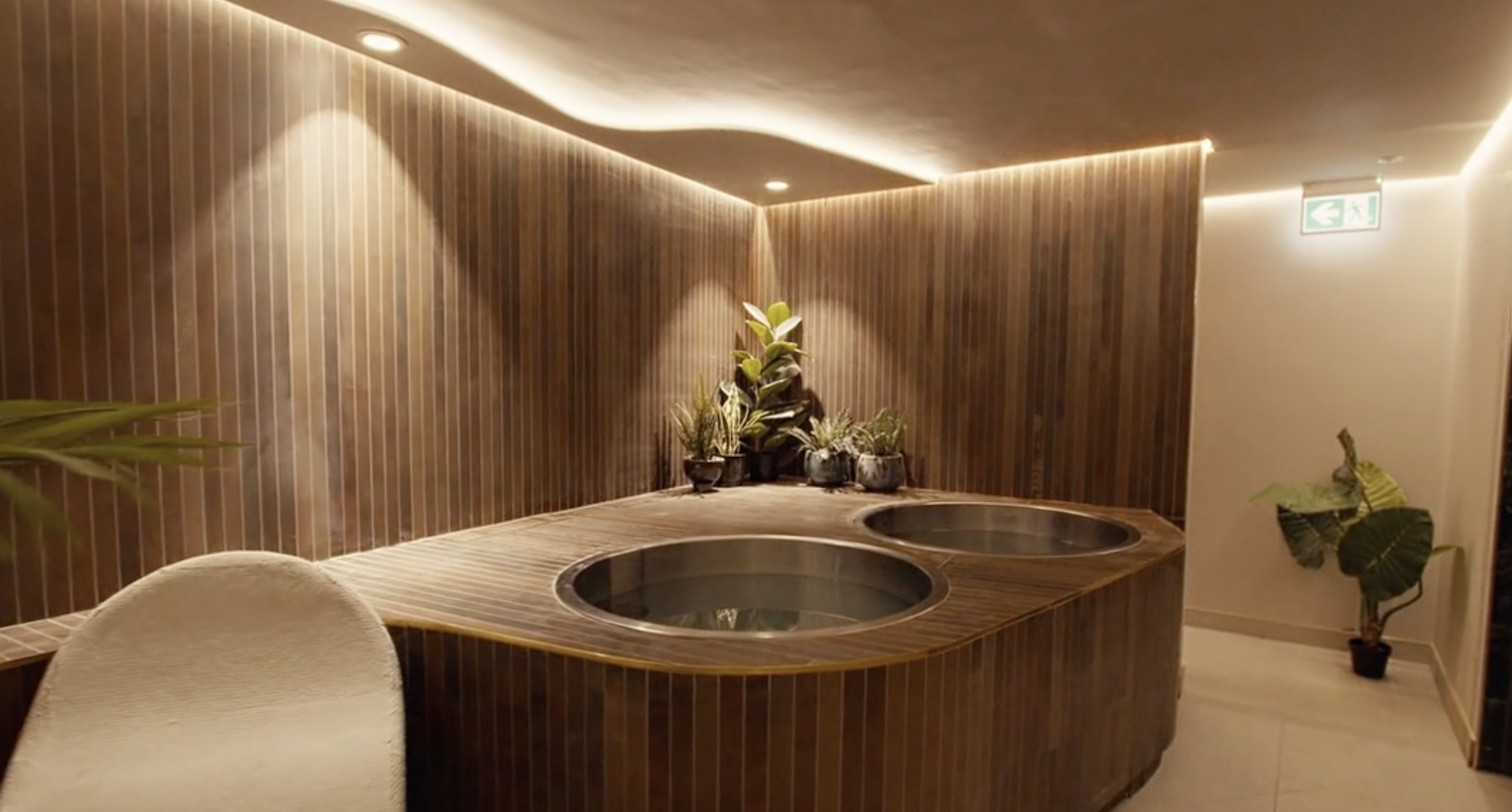 Indoor spa area with two round kooled ice bath tubs, wooden wall paneling, and potted plants.