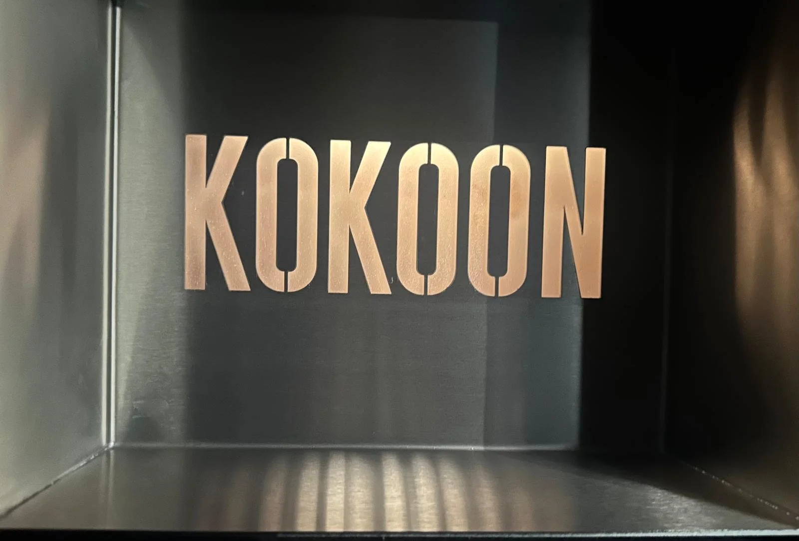 Inside a metallic box, the word KOKOON is spelled out in large, bold, copper-colored letters.