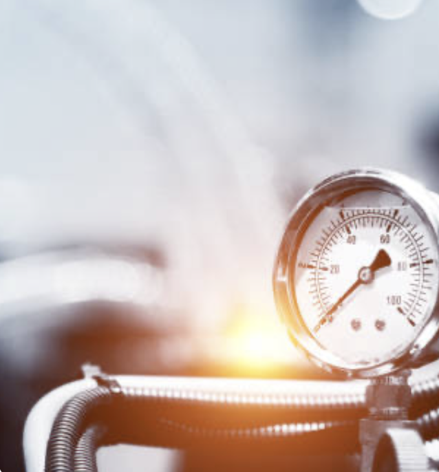 Close-up of a pressure gauge attached to a pipe or machine, with a slight glow or light effect in the background.