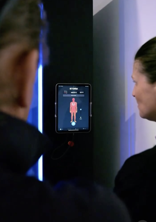 Two people look at a screen displaying a human body and temperature information in a dark room.